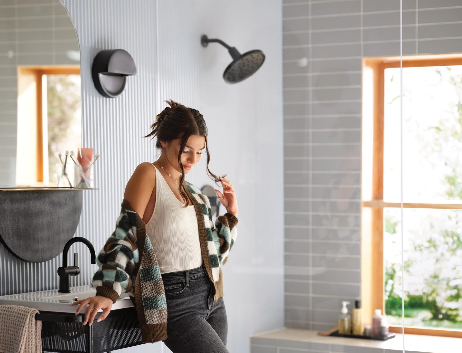 Matte black round rainshower head mounted on ceiling with curved arm in modern bathroom.