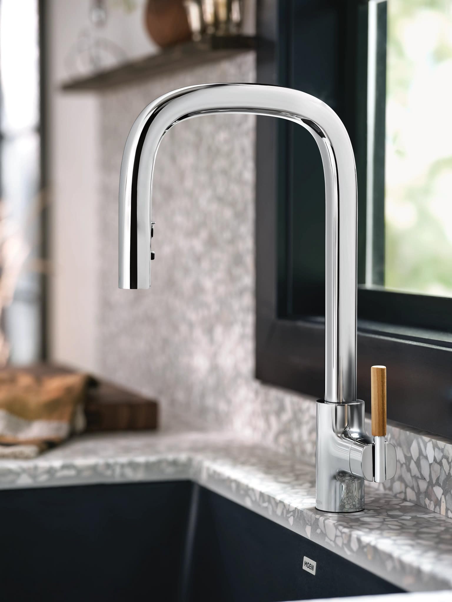 Chrome pulldown kitchen faucet with single handle and wooden accent lever mounted on countertop above sink.