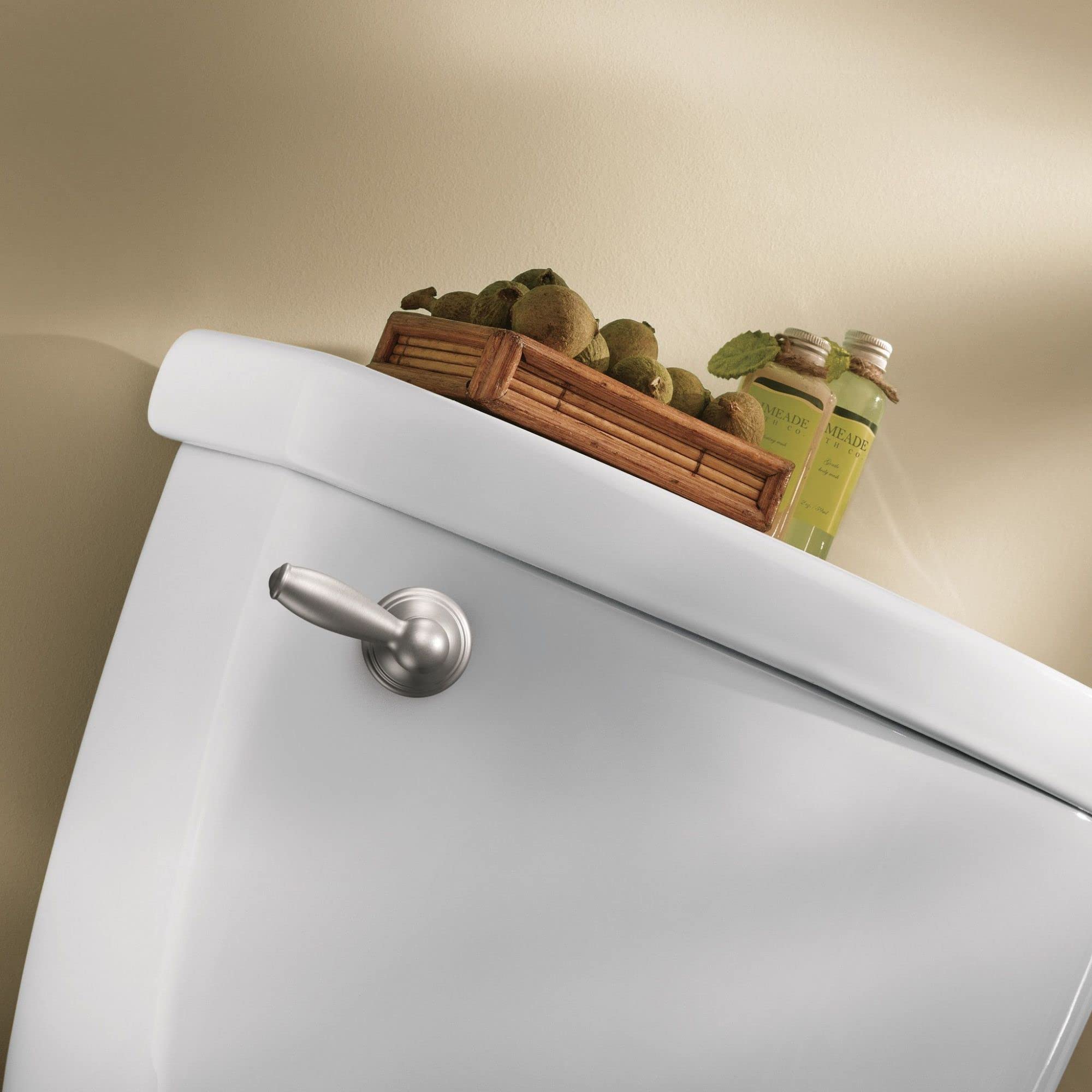 Brushed nickel toilet tank lever handle mounted on white porcelain toilet tank.