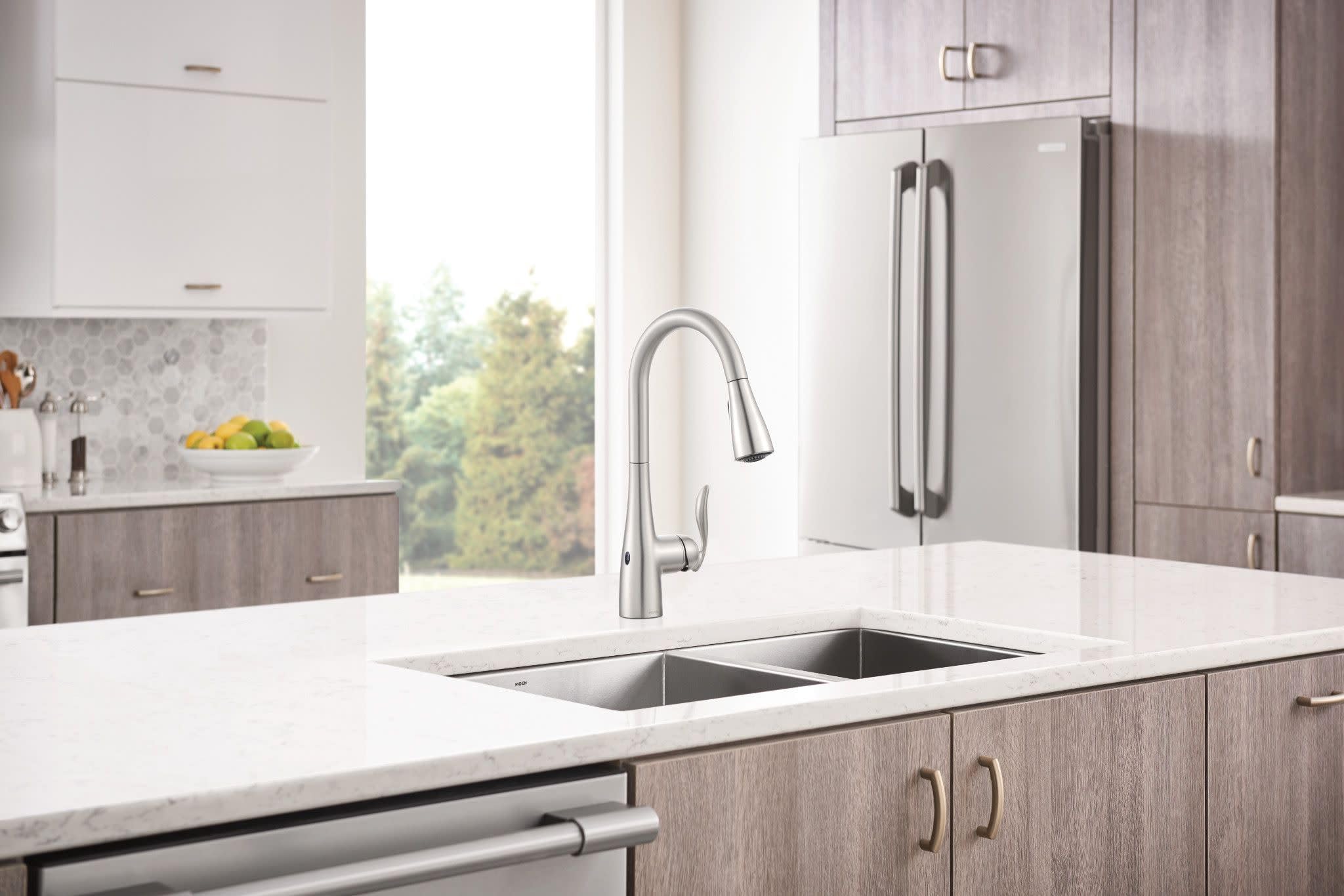 Stainless steel pull-down kitchen faucet with curved spout installed above double sink in modern kitchen.