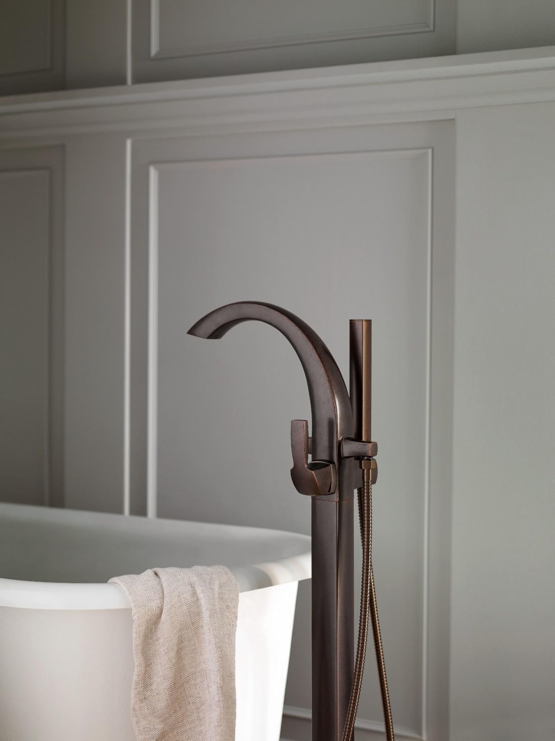 Oil rubbed bronze freestanding tub filler with curved spout, single handle, and detachable handshower on hose.