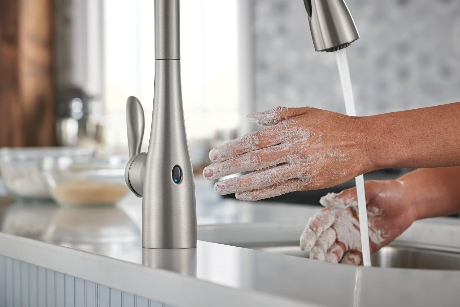 Stainless steel pull-down kitchen faucet with touchless sensor activated by hands being washed under running water.