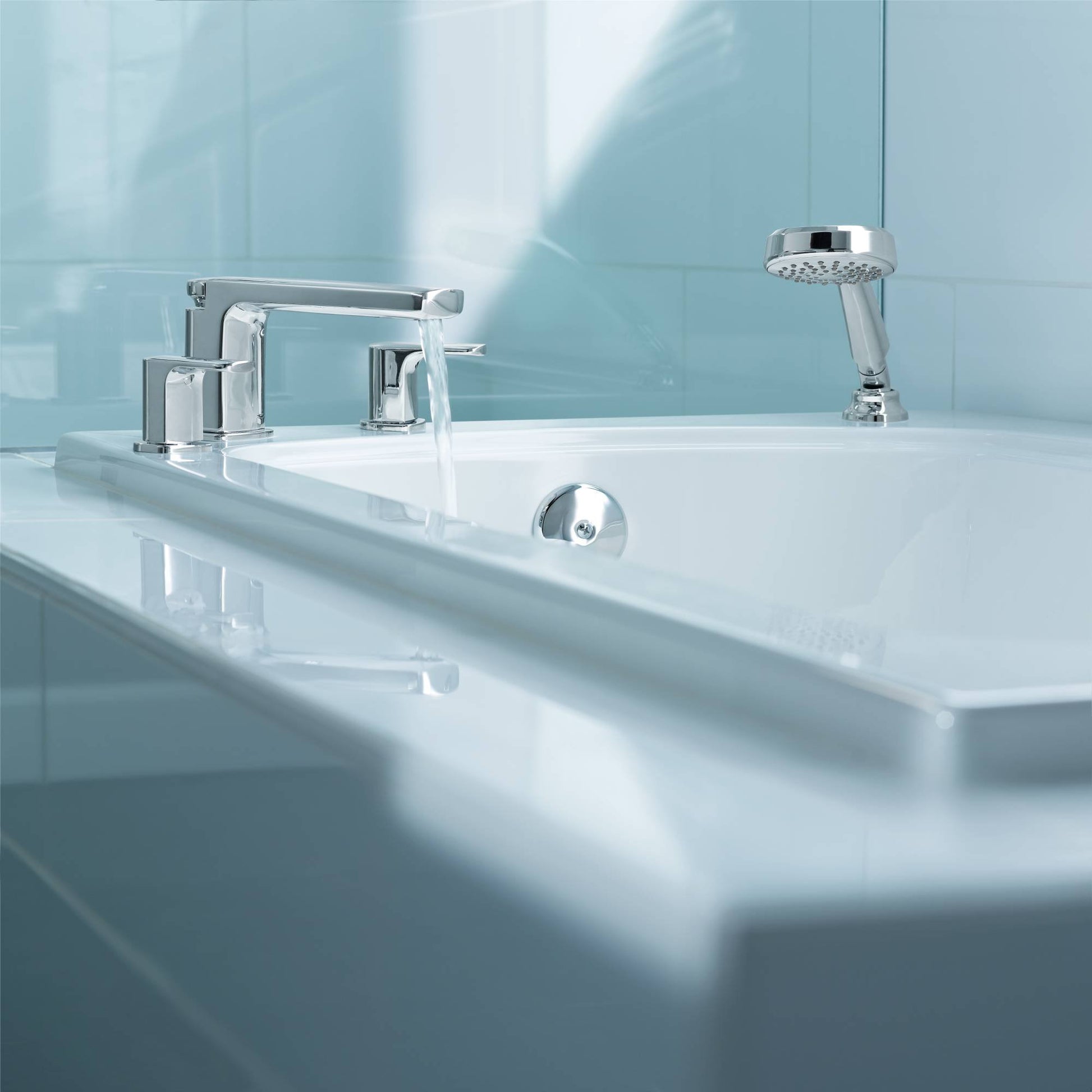 Chrome two-handle low arc roman tub faucet with hand shower and control valve mounted on white bathtub rim.