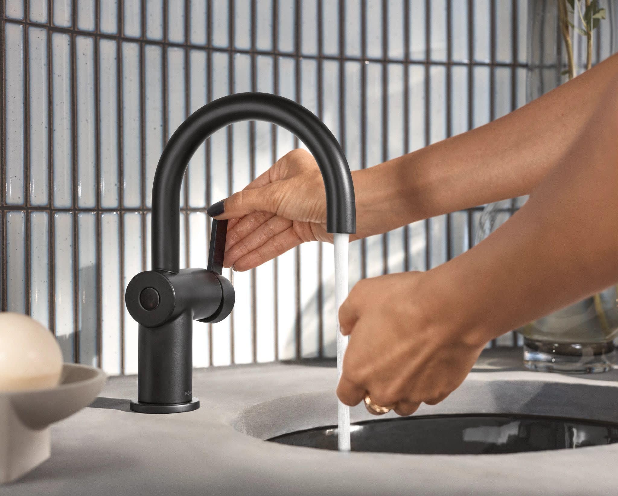 Matte black single-handle bathroom faucet with curved spout and sensor activation, shown with hand under running water.