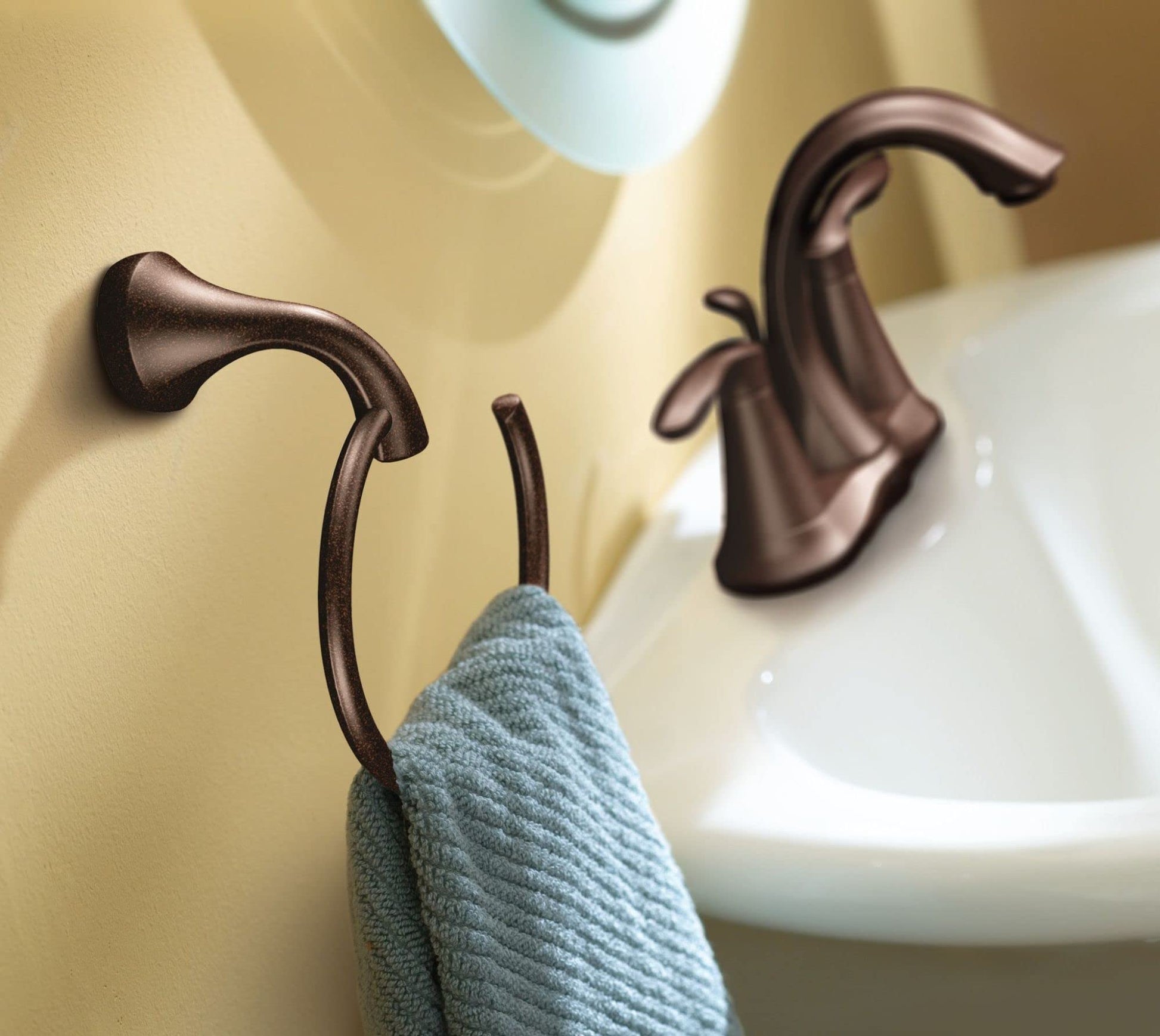Oil rubbed bronze towel ring mounted on bathroom wall with blue-gray towel draped over curved hook.