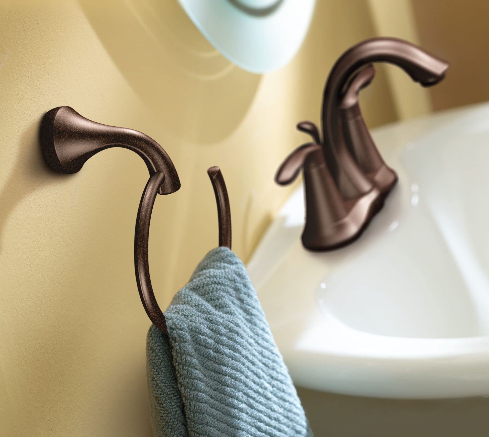 Oil rubbed bronze towel ring mounted on bathroom wall with blue-gray towel draped over curved hook.
