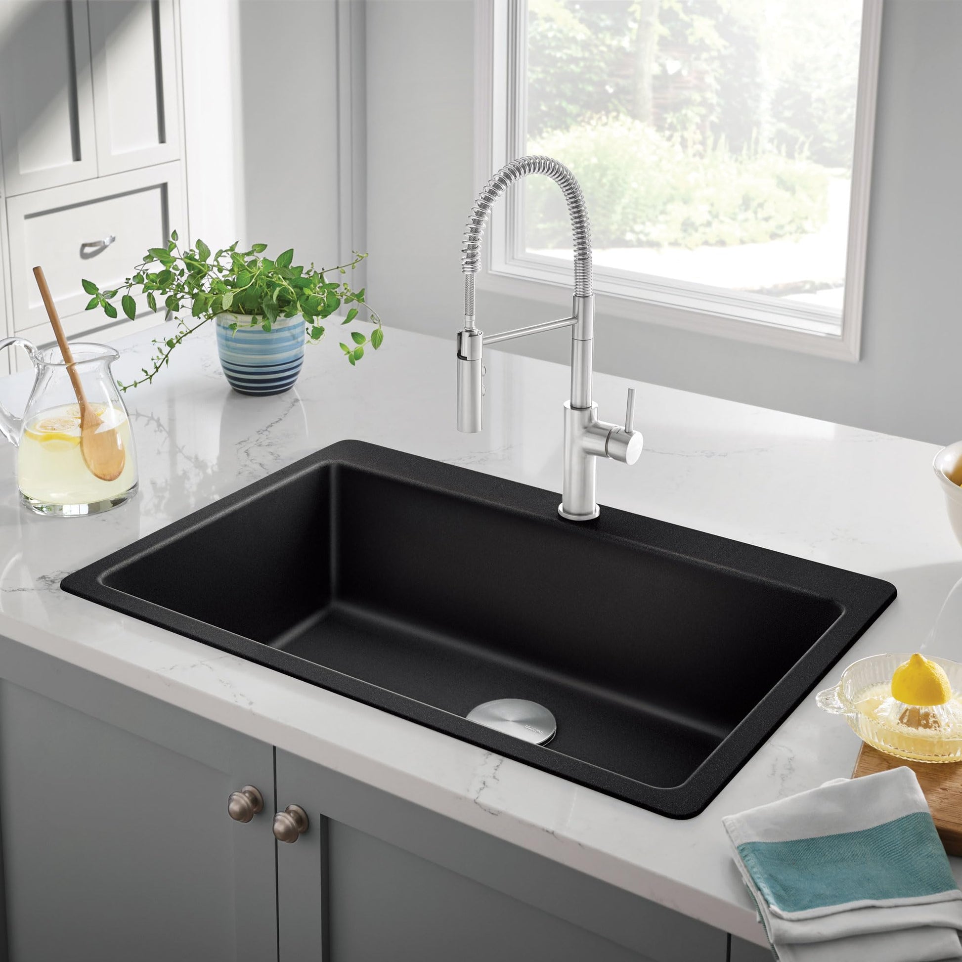 Coal black single bowl kitchen sink with chrome pull-down faucet installed in white countertop.
