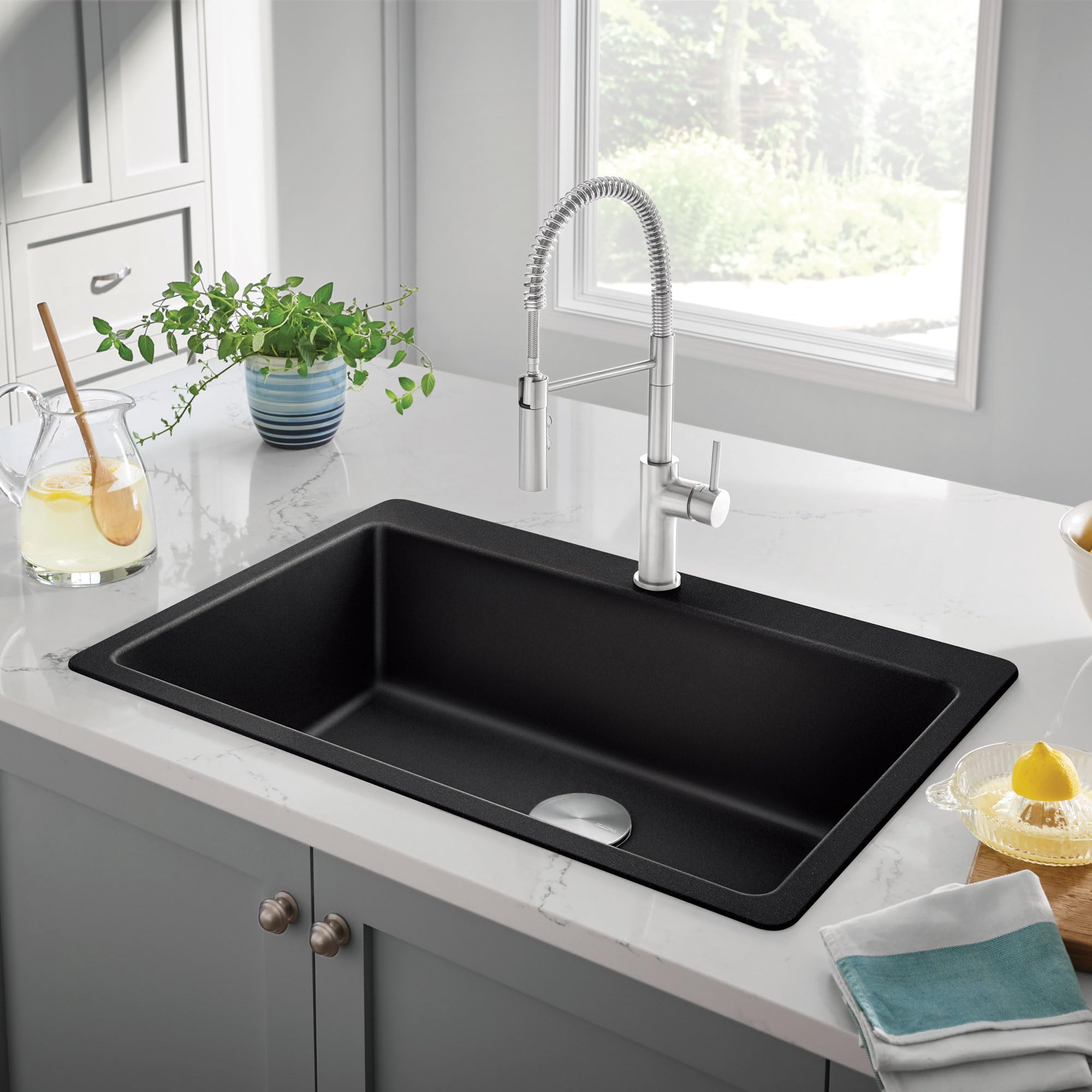 Coal black single bowl kitchen sink with chrome pull-down faucet installed in white countertop.