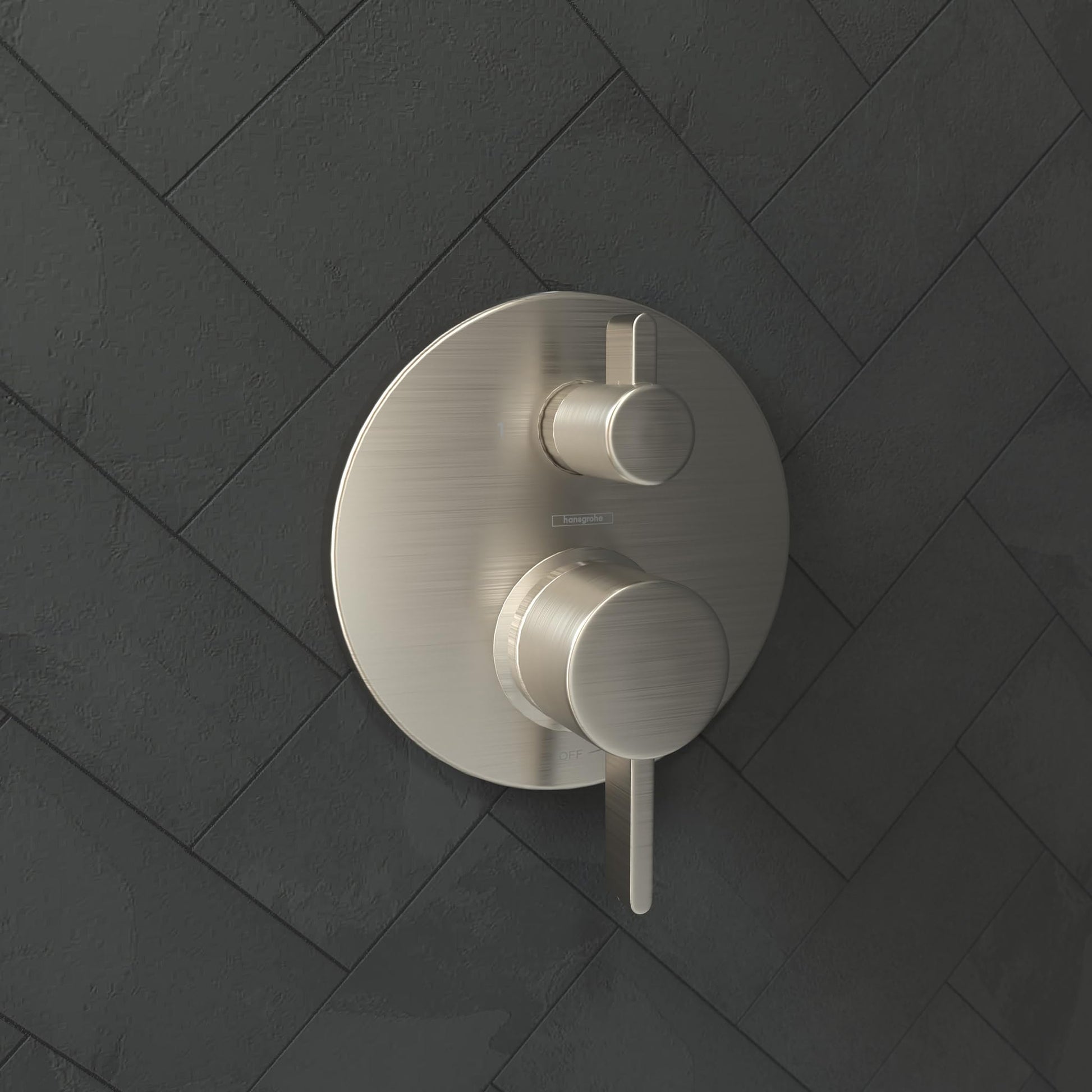 Brushed nickel shower trim with round escutcheon plate and two cylindrical control handles mounted on tile wall.