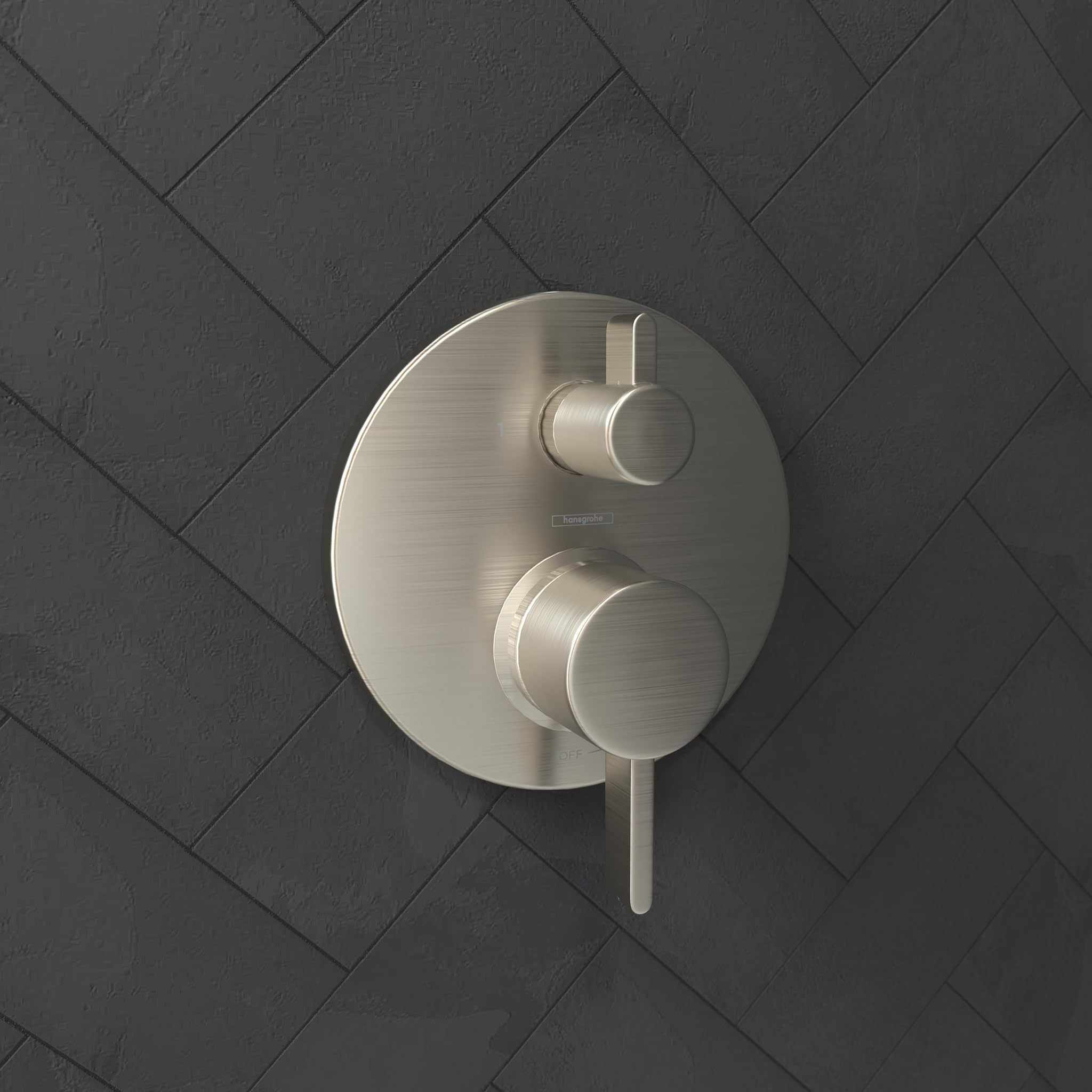 Brushed nickel shower trim with round escutcheon plate and two cylindrical control handles mounted on tile wall.