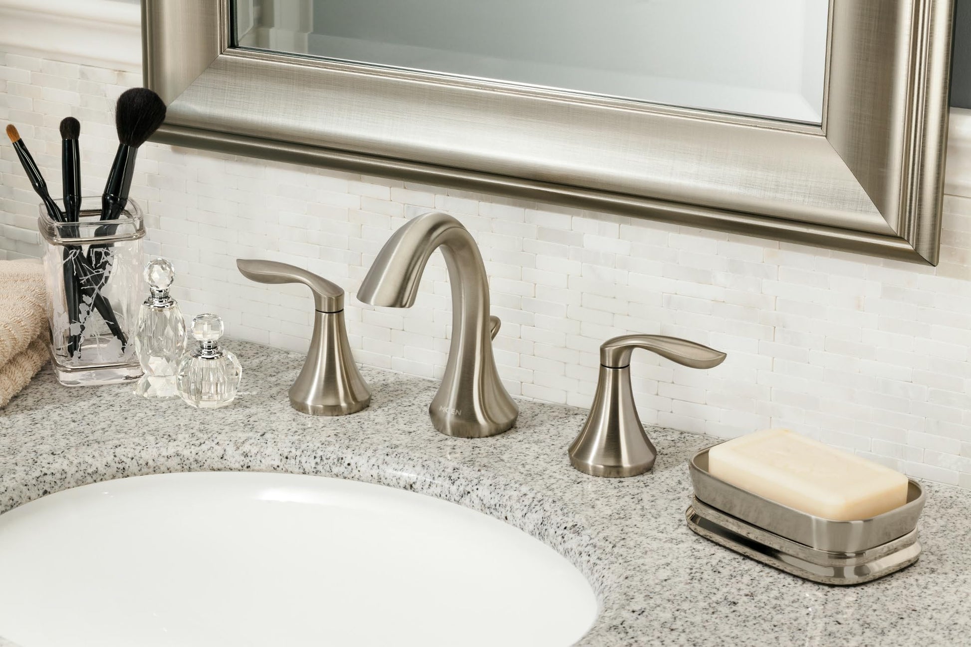 Brushed nickel two-handle widespread bathroom faucet with curved spout installed on granite countertop.
