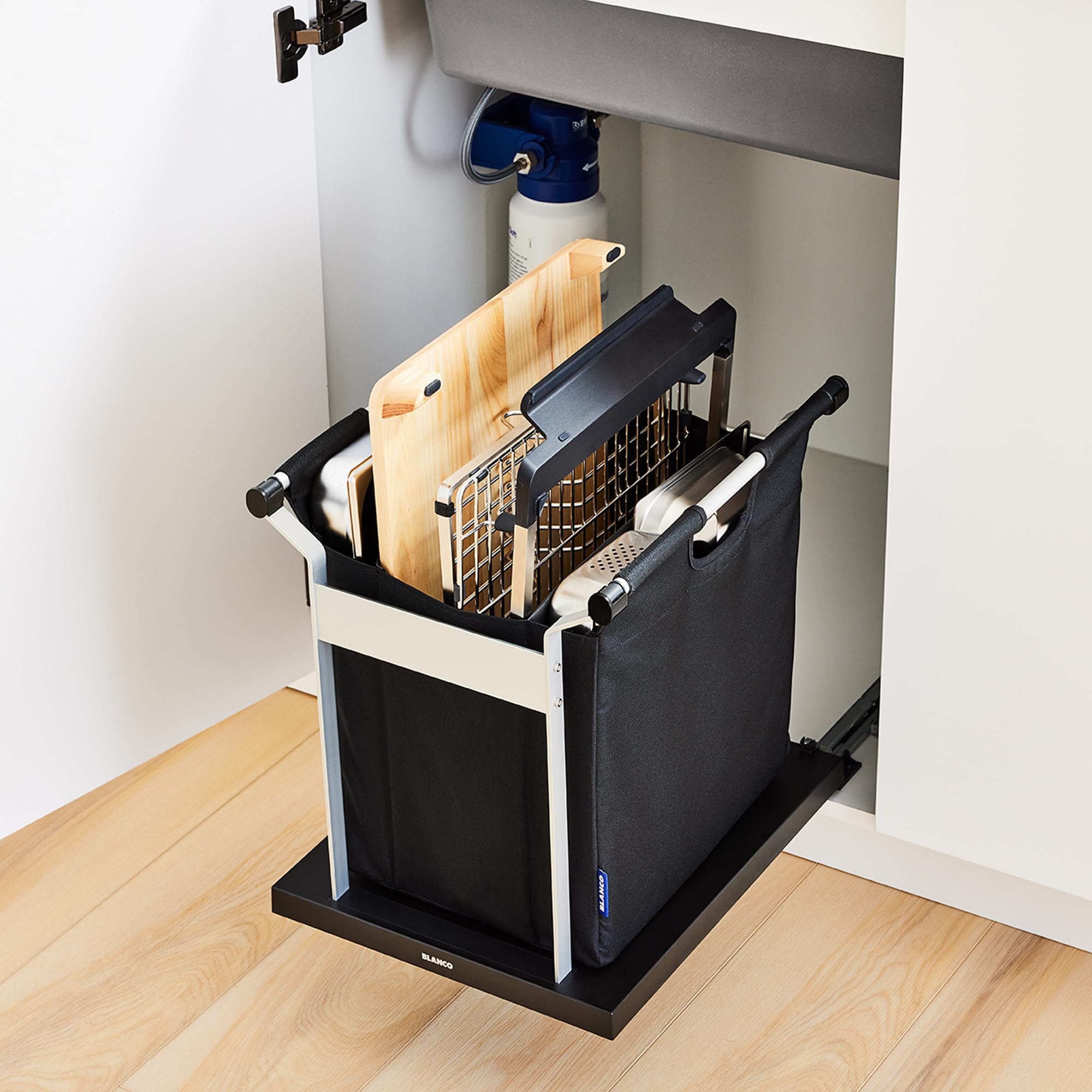 Black and white sink storage organizer with wooden cutting board, metal mesh basket, and white handles installed under kitche