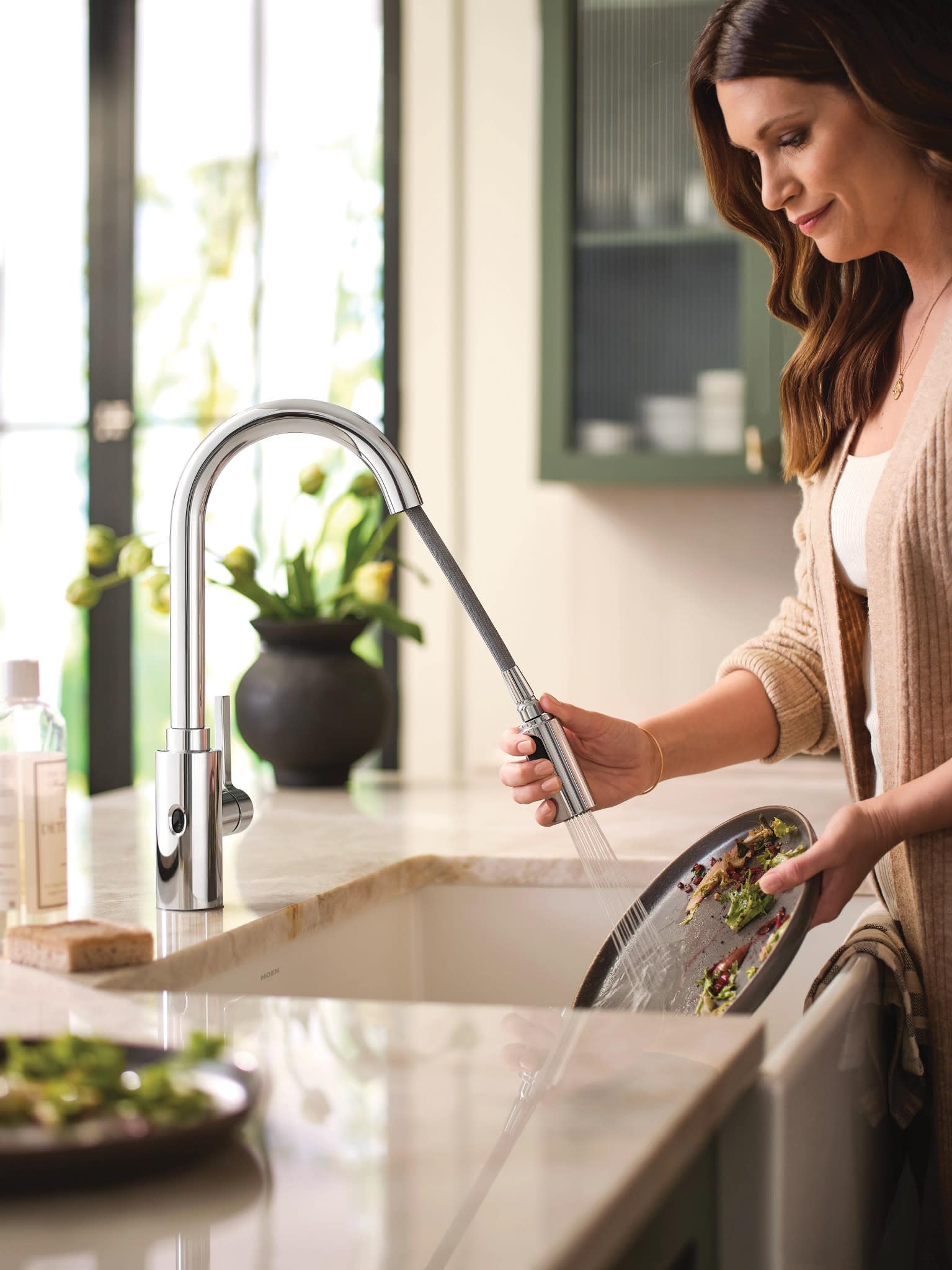 Chrome kitchen faucet with high arc pulldown spout and touchless sensor being used to rinse vegetables.