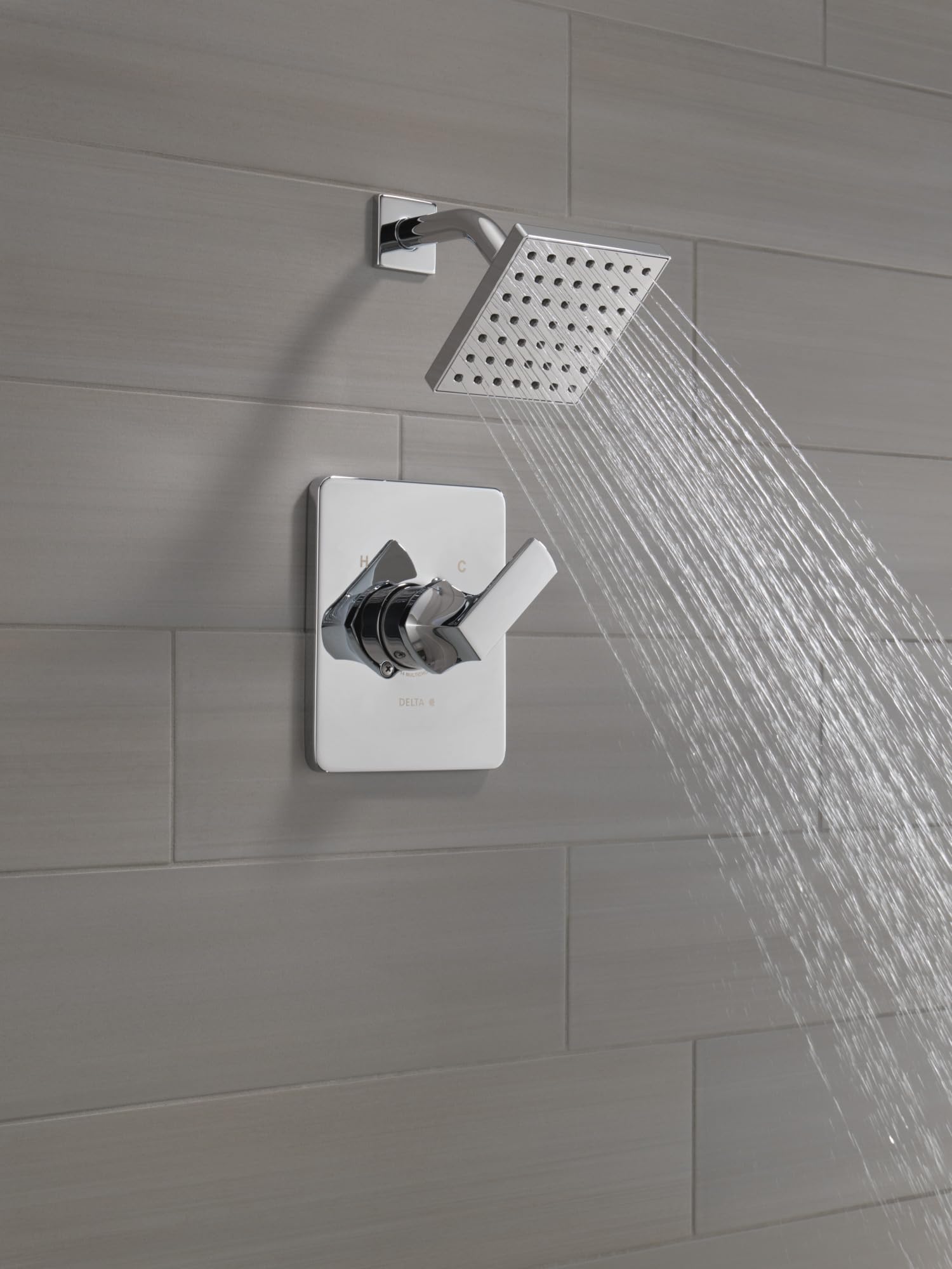 Chrome shower trim with square rainfall showerhead and white rectangular valve body mounted on gray tile wall.