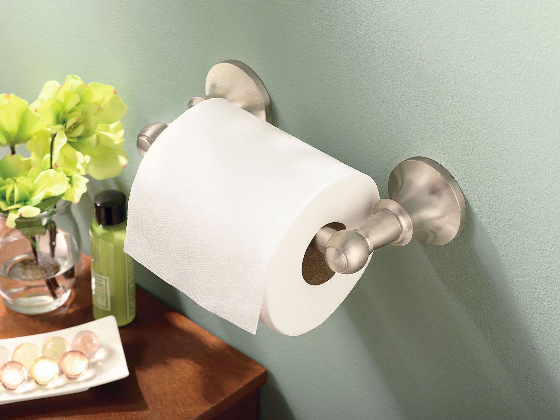 Brushed nickel toilet paper holder mounted on green wall with white paper roll installed.
