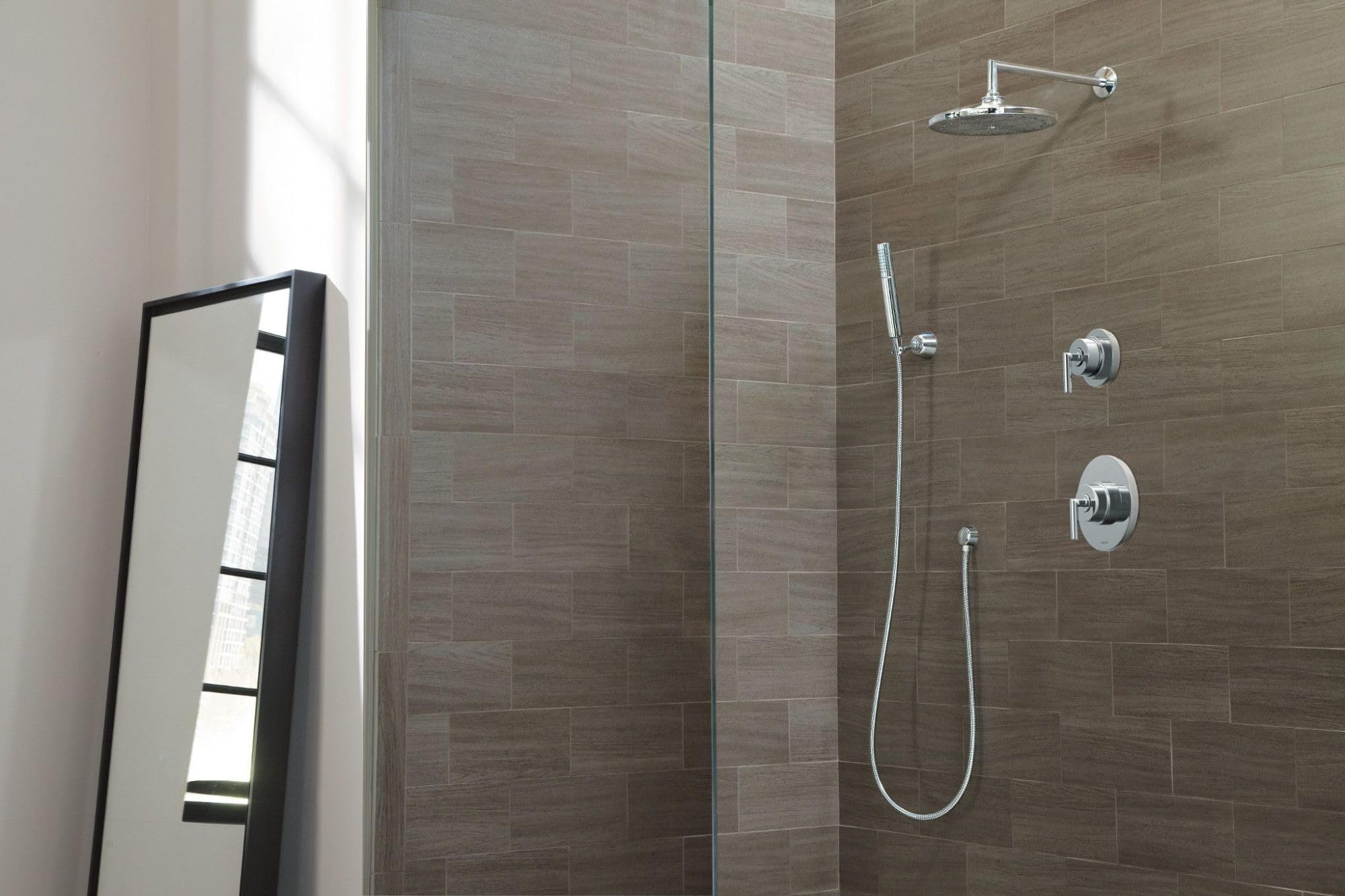 Chrome handheld shower head with hose and wall mount in tiled shower enclosure.