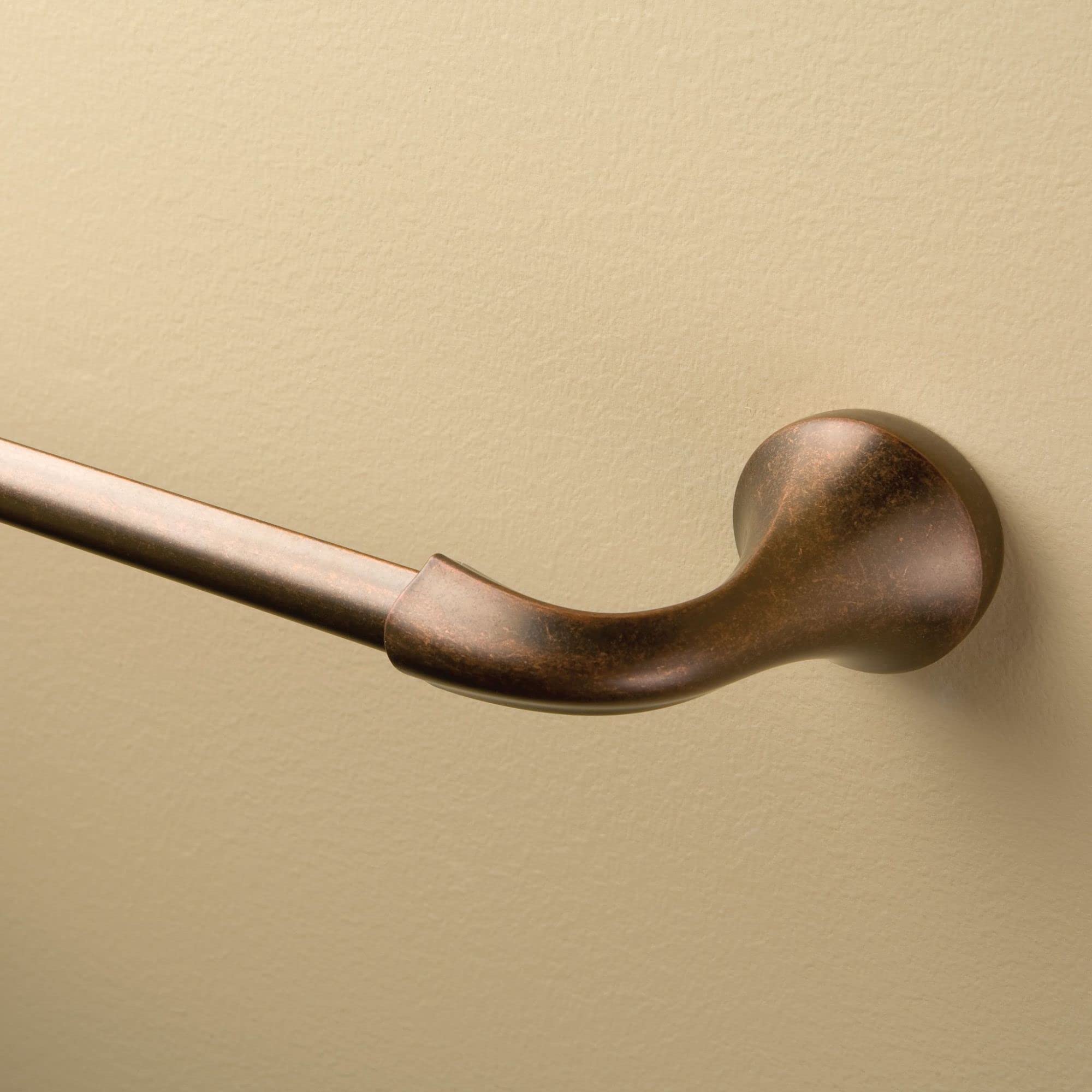 Oil rubbed bronze curved towel bar mounted on beige wall with spherical end cap.