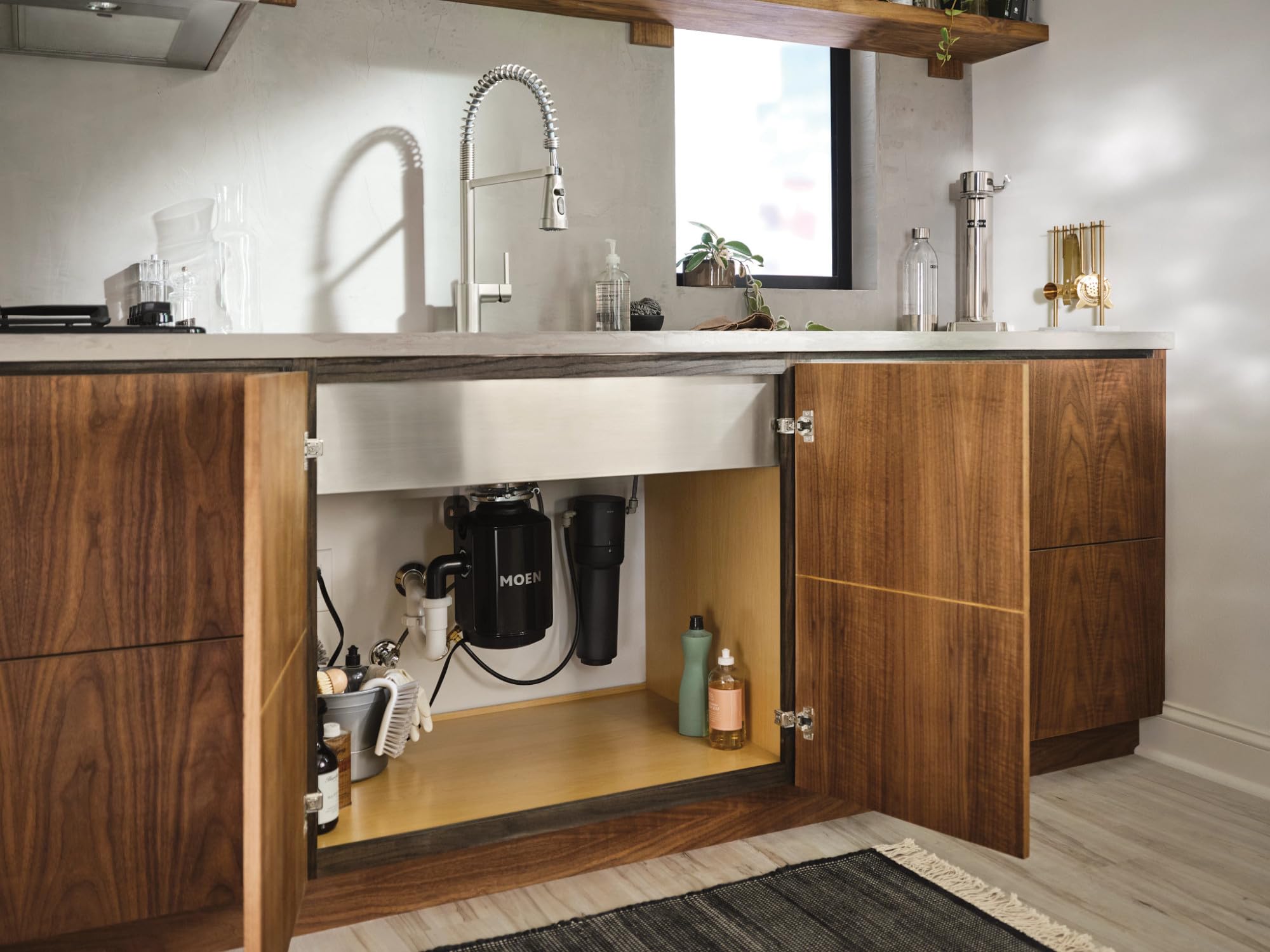 Chrome Moen under-sink water filtration system with black filter cartridges installed beneath farmhouse sink.