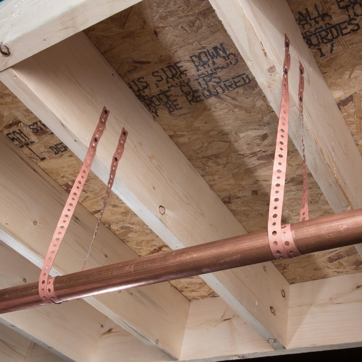 Steel pipe securing straps with perforated metal bands securing copper pipe to wooden ceiling joists.