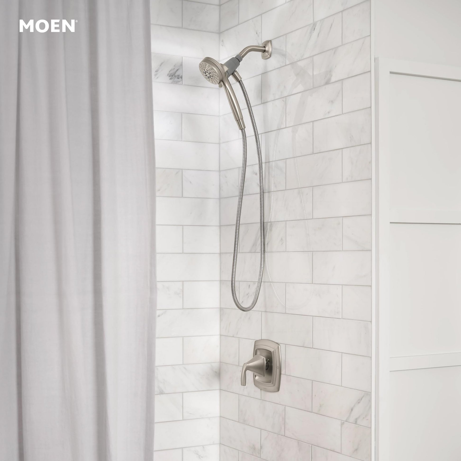 Brushed nickel hand shower with flexible hose and wall-mounted control valve in marble tile shower.