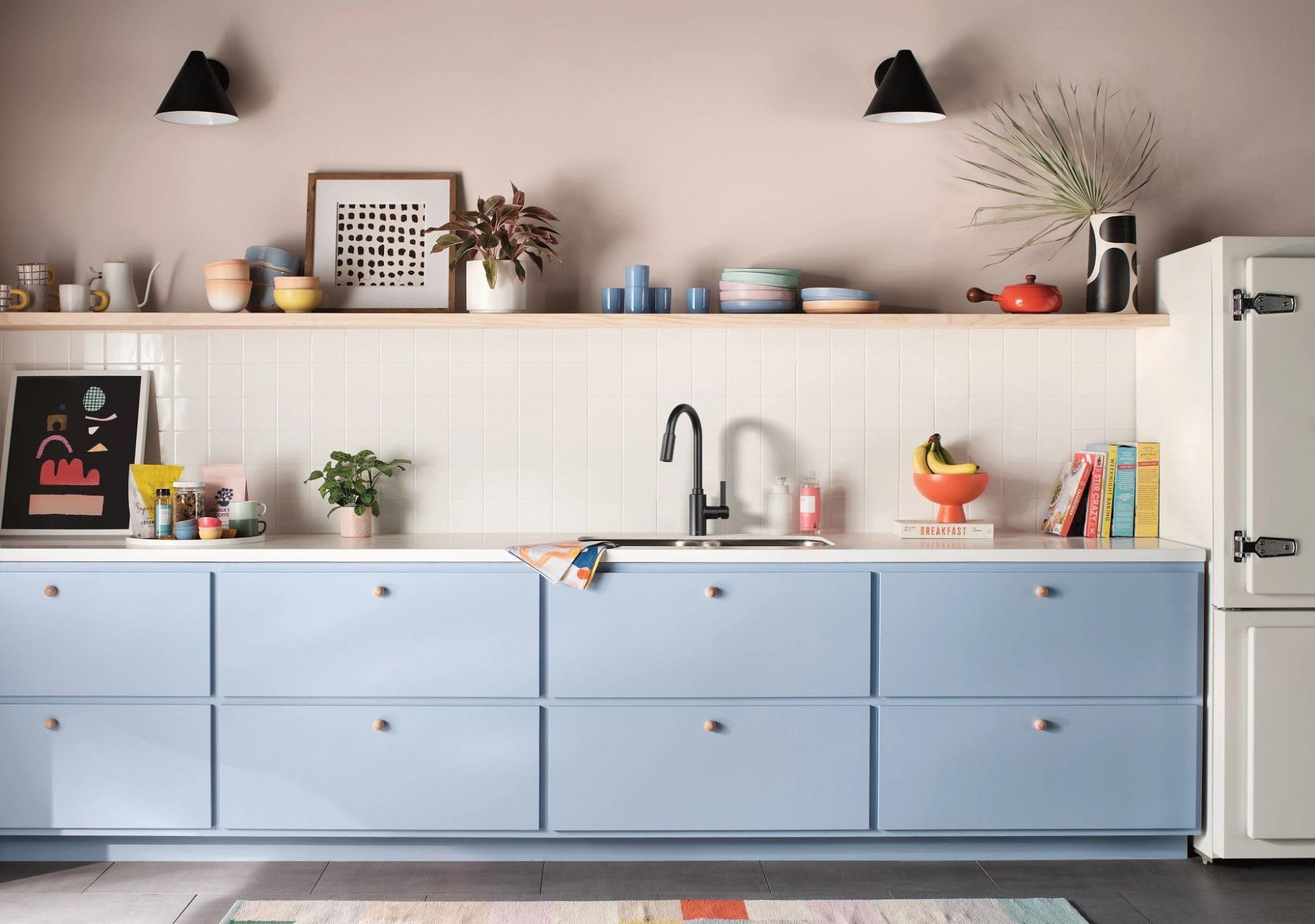 Matte black single-handle kitchen faucet with pull-down sprayer mounted on white sink with blue cabinetry.