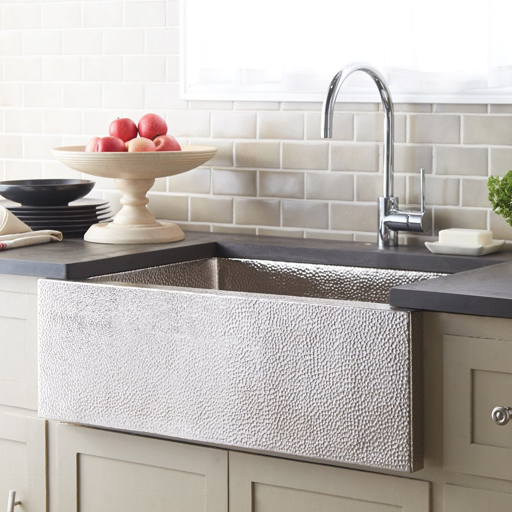 Brushed nickel apron-front kitchen sink with hammered copper interior and curved faucet in countertop setting.