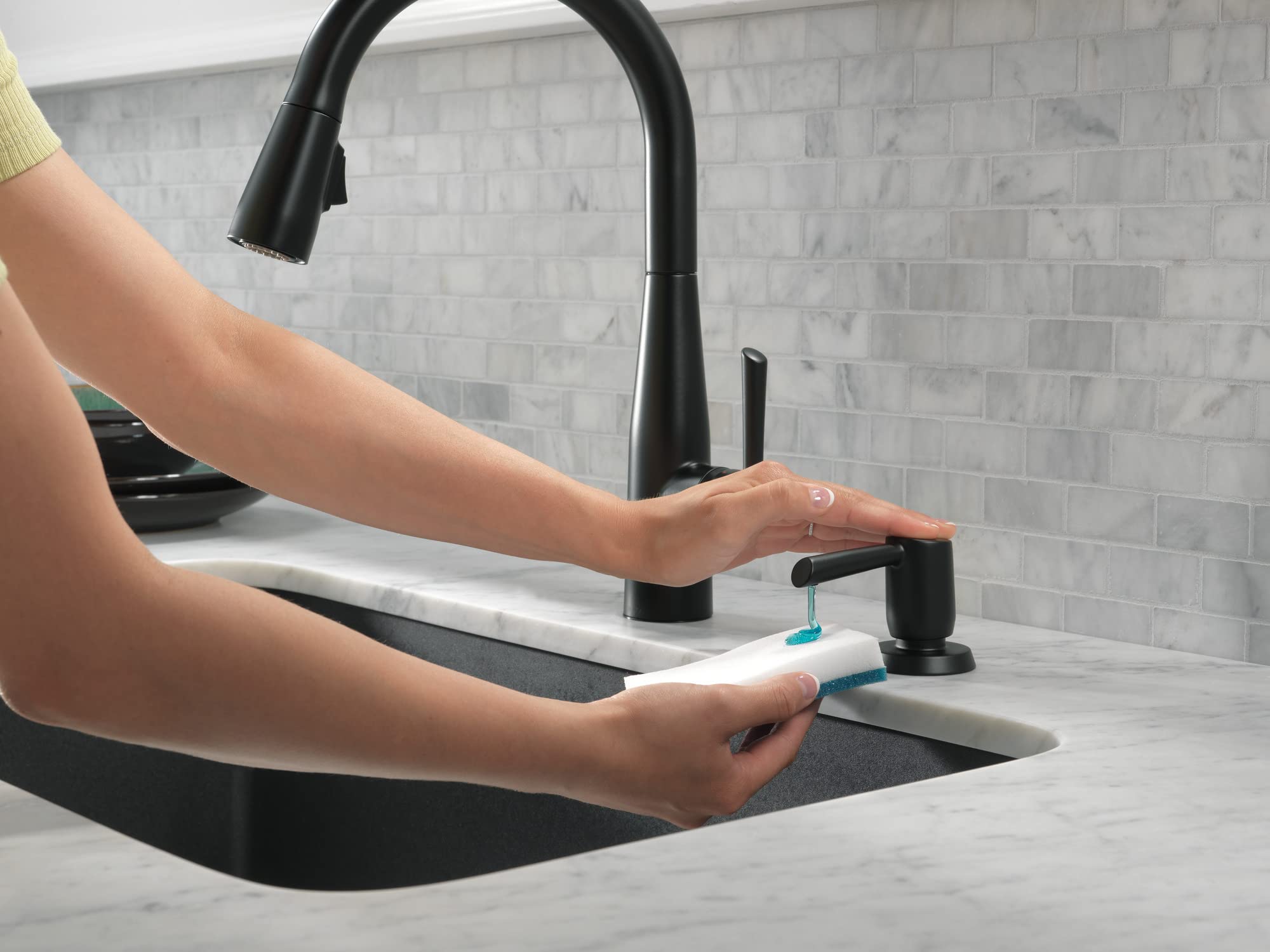 Matte black metal soap dispenser with pump mounted next to kitchen faucet on countertop.