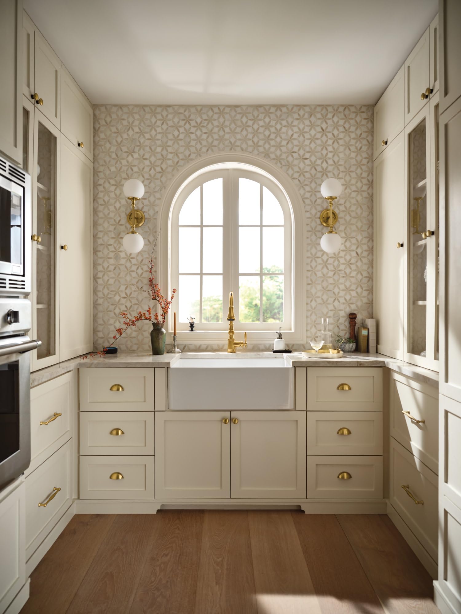 White fireclay apron front sink with single bowl installed in cream cabinetry beneath arched window.