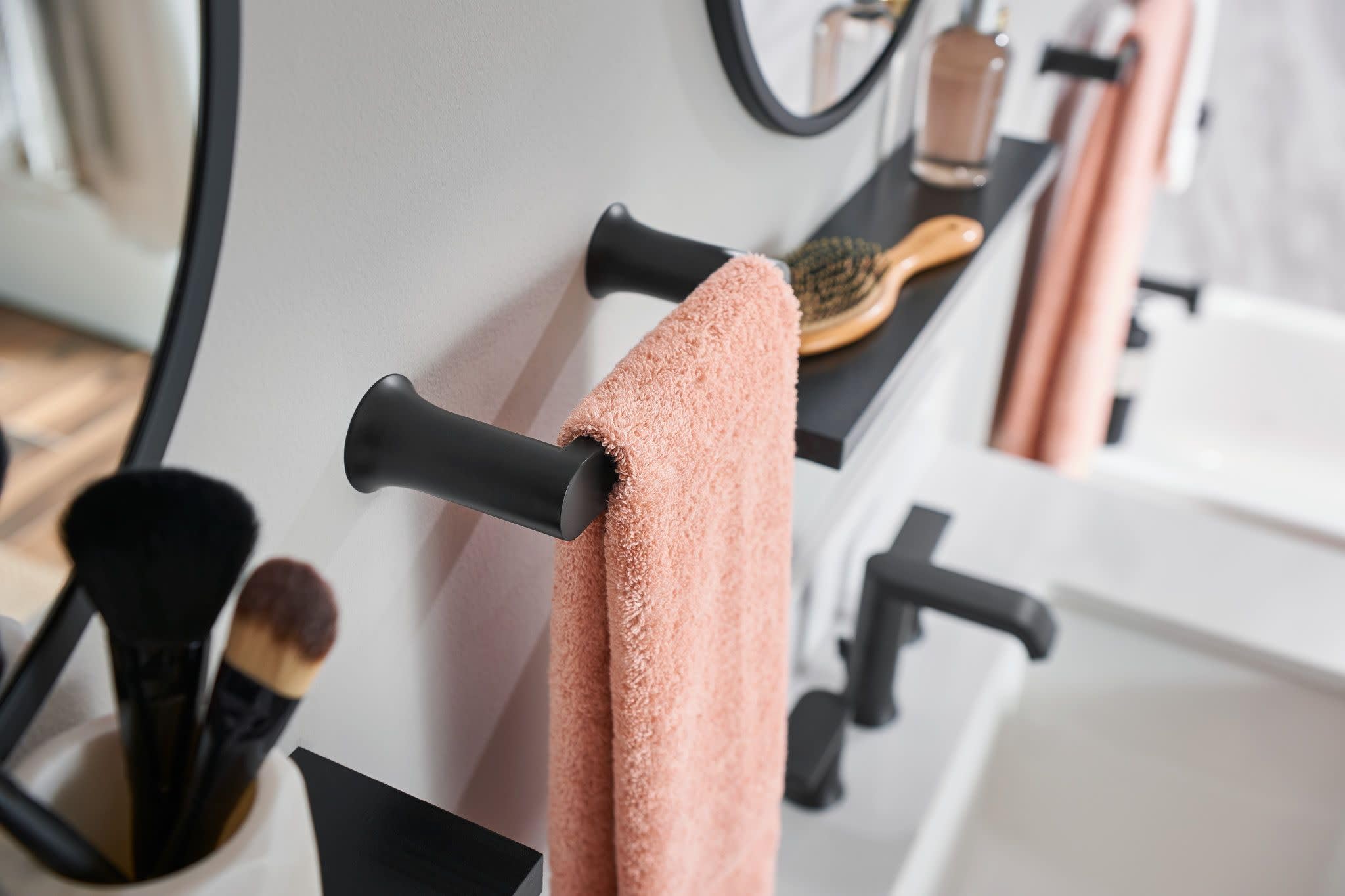 Black metal hand towel bar with cylindrical ends holding a pink towel on bathroom wall.