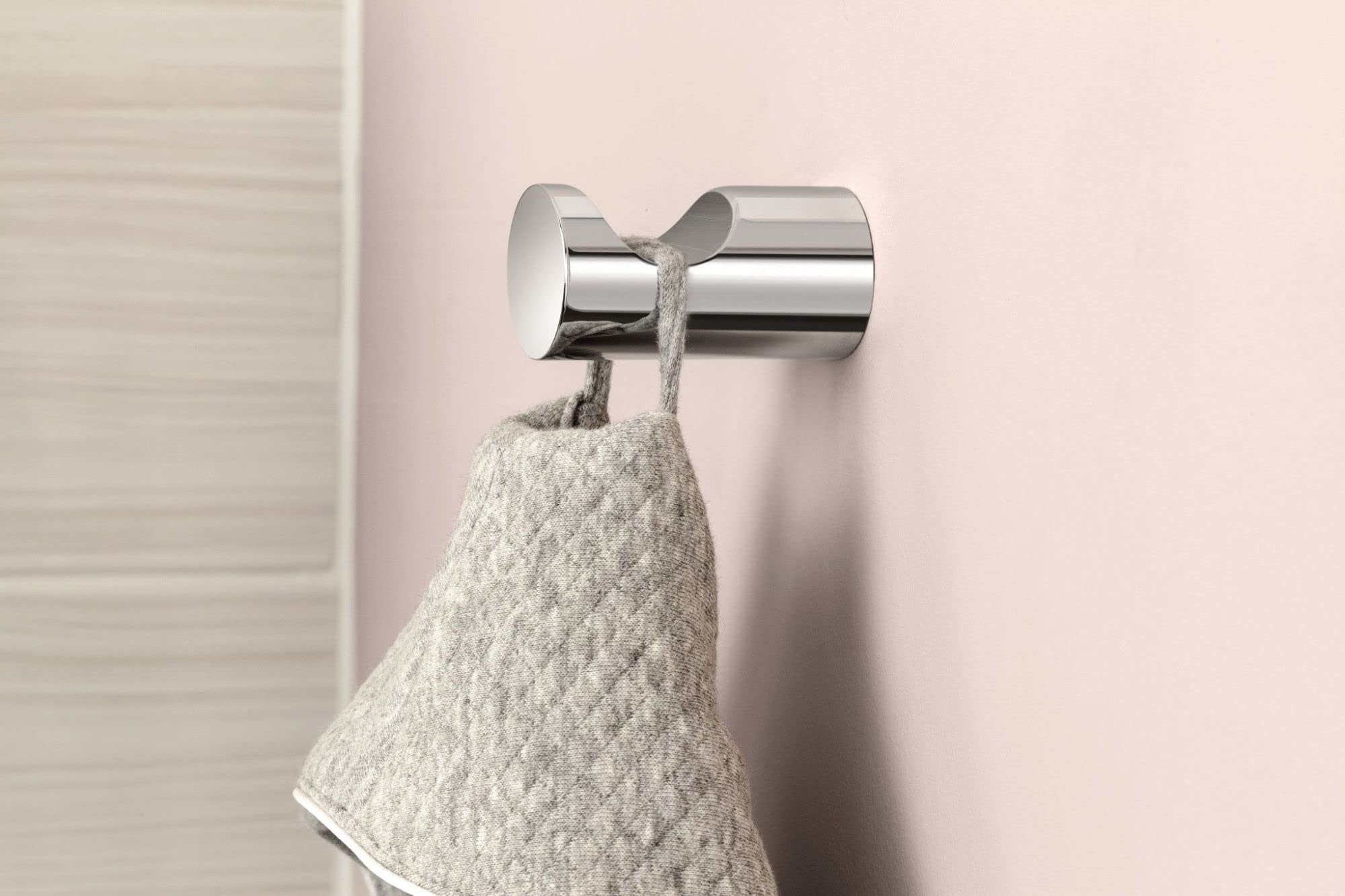 Chrome robe hook with cylindrical design holding a light gray towel against a pink wall.
