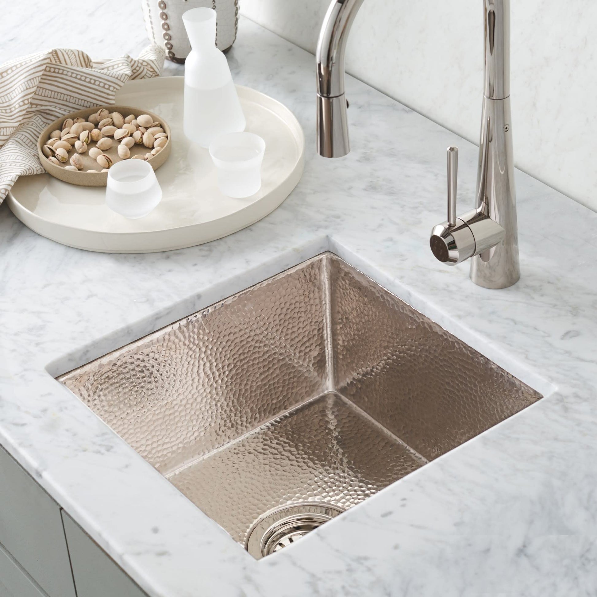 Polished copper square prep sink with divided compartments and hammered texture, installed in marble countertop with stainles