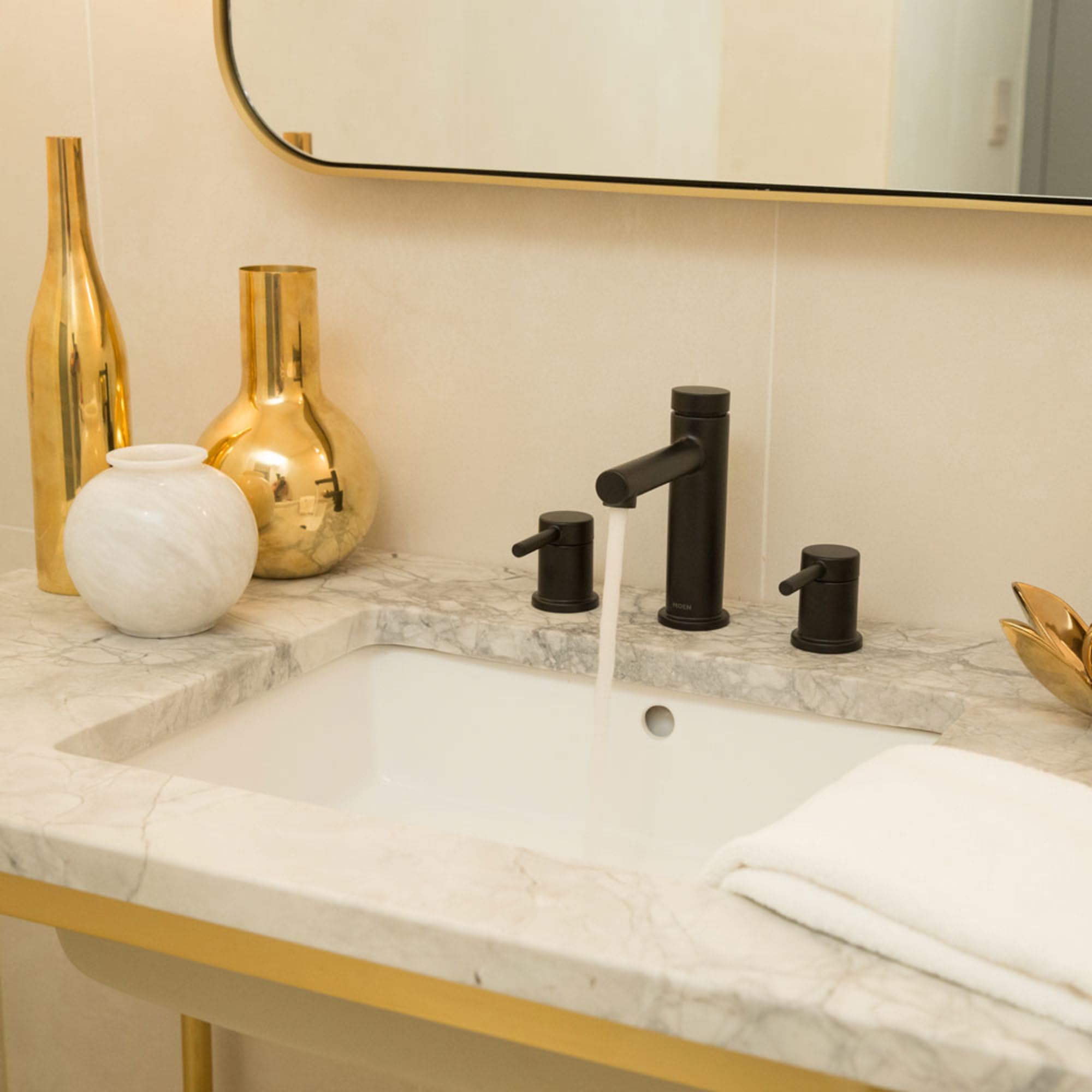 Matte black widespread bathroom faucet with two handles installed on white marble countertop above sink.