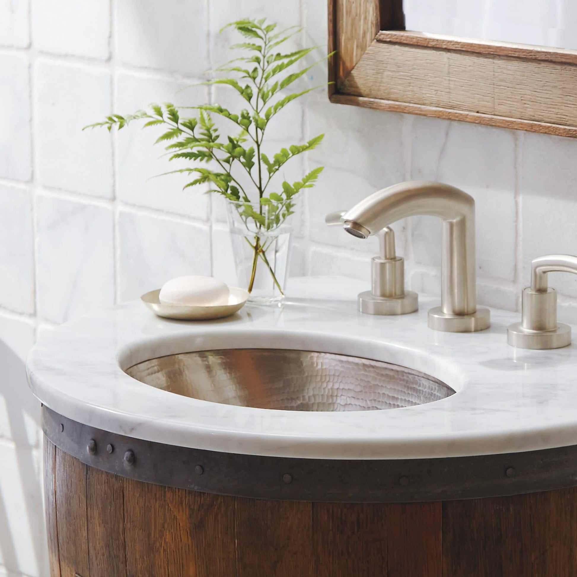 Polished nickel faucet with curved spout and dual handles mounted on white marble countertop with copper sink basin.
