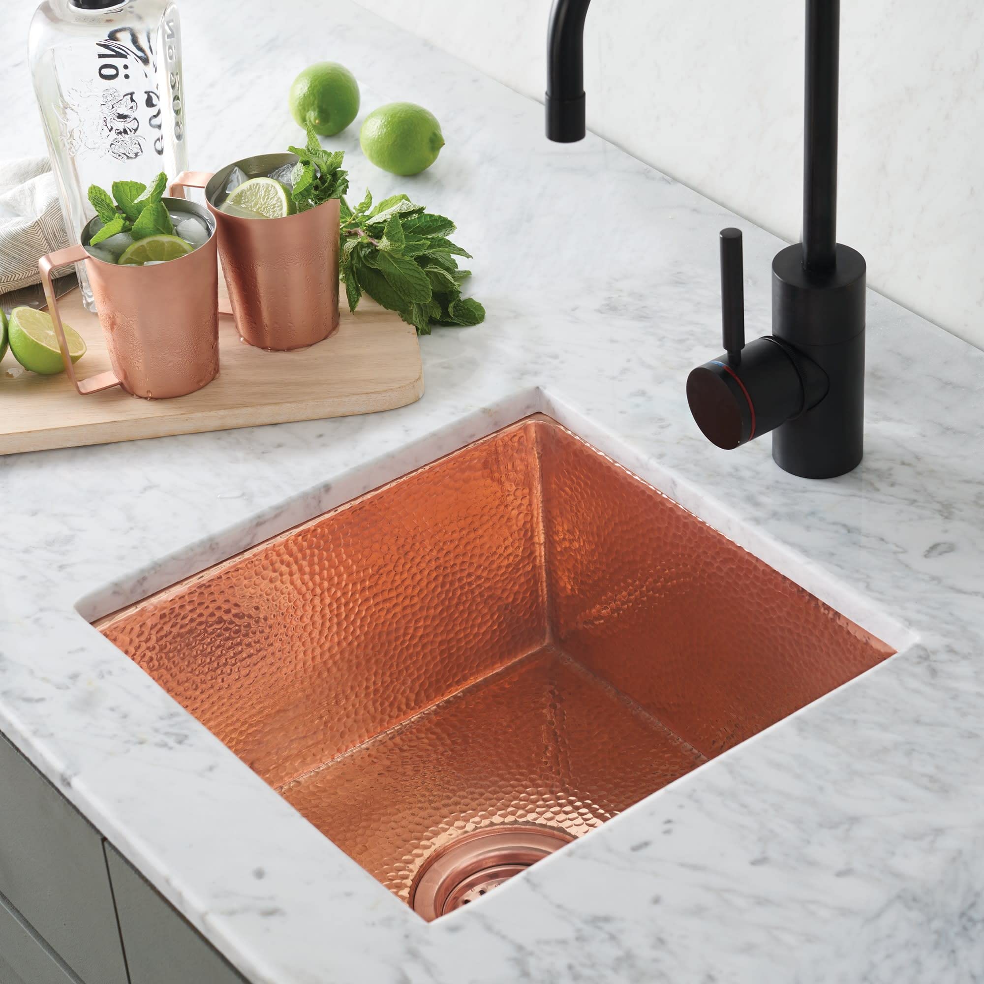 Polished copper prep sink with hammered texture in marble countertop, black faucet visible.