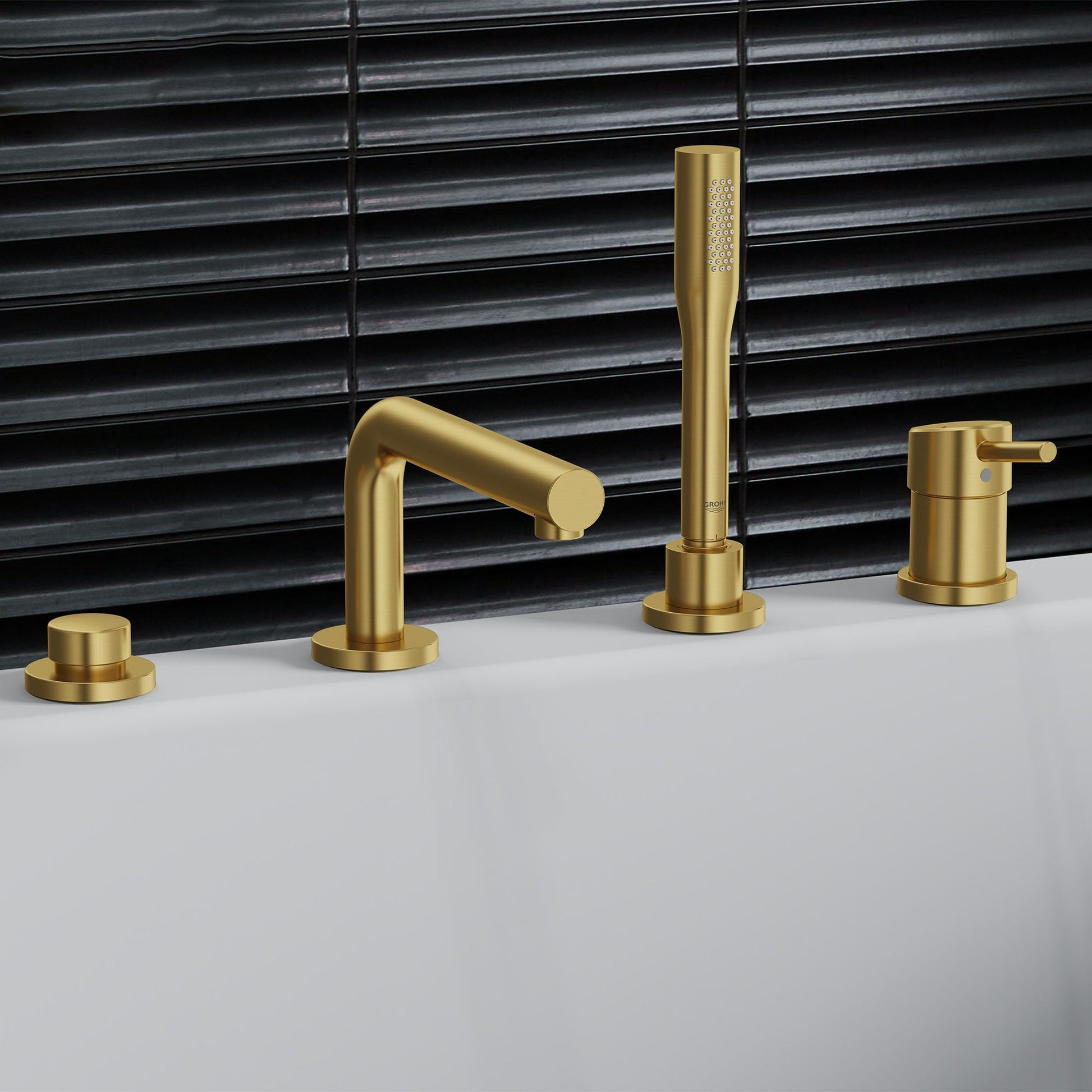 Brushed gold four-hole deck mount Roman tub faucet with single handle, hand shower, and matching control knobs on white surfa