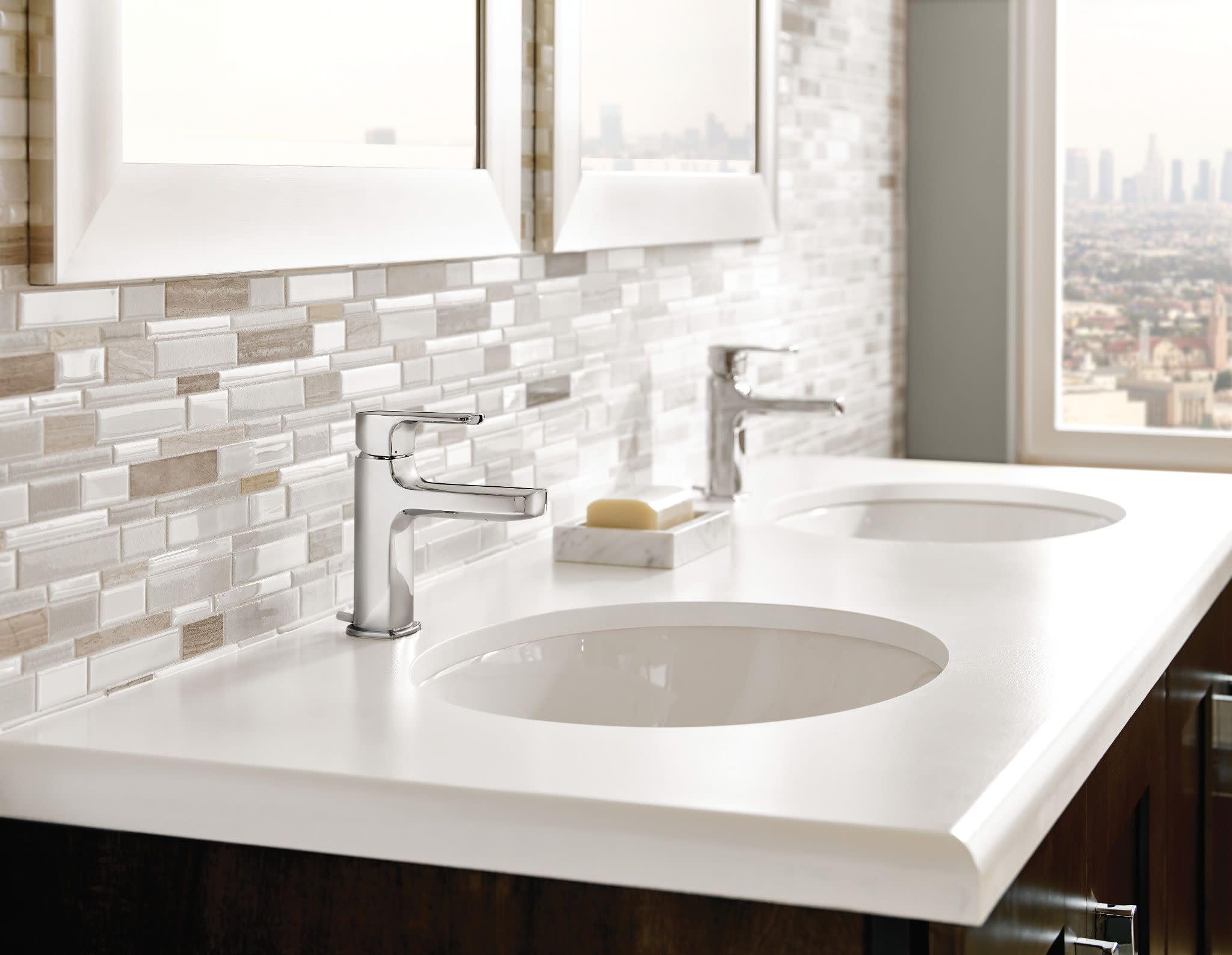 Chrome two-handle widespread bathroom faucet with curved spout installed on white vanity with dual round sinks.