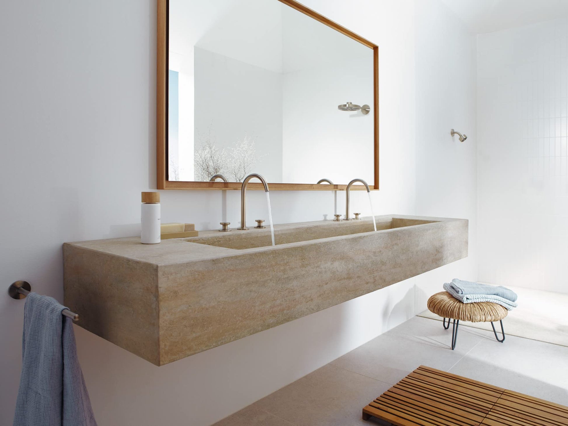 Brushed nickel shower head mounted on white bathroom wall above concrete sink vanity.