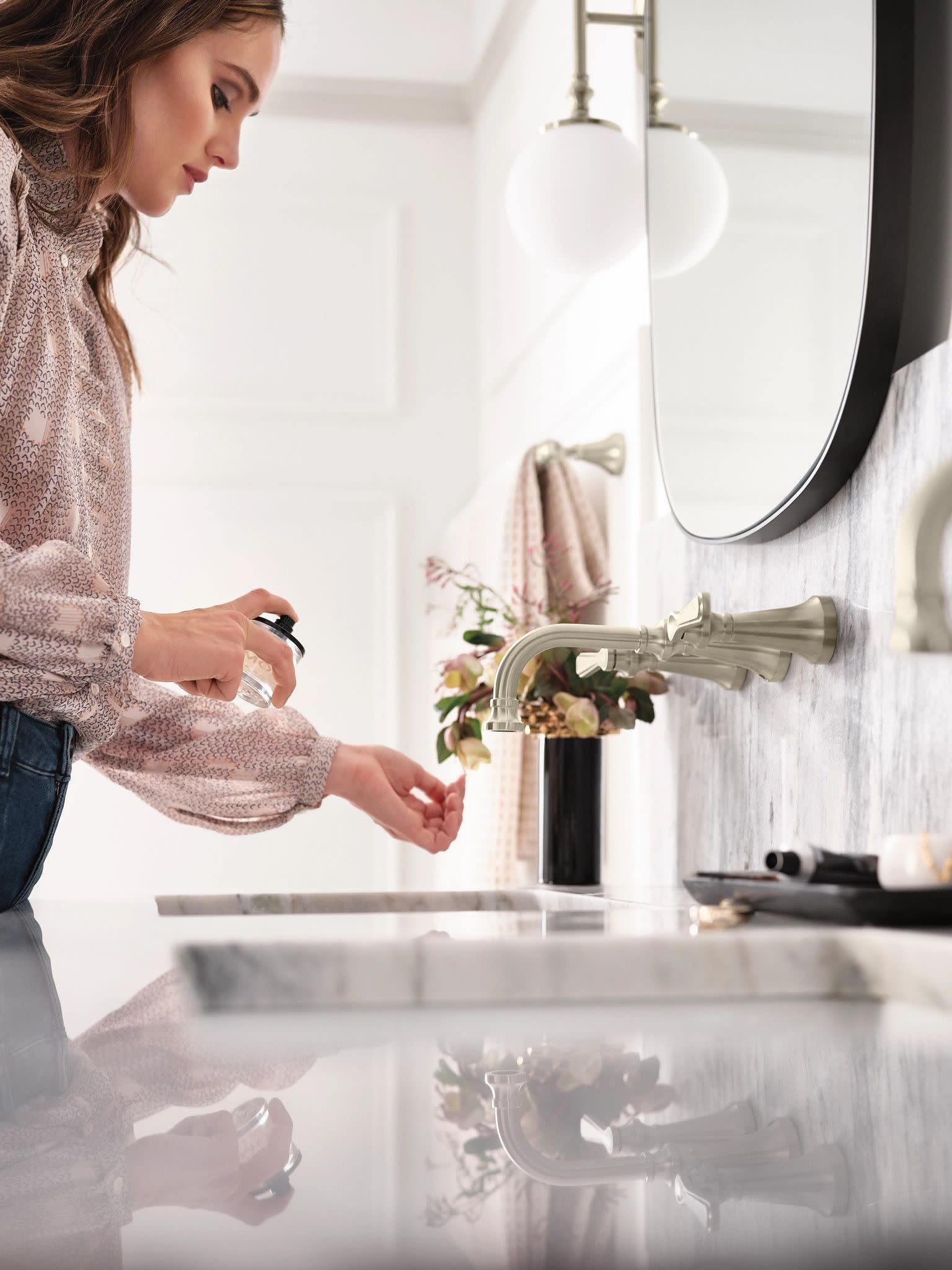 Brushed nickel wall-mount bathroom faucet with traditional lever handle mounted above white sink in bathroom.