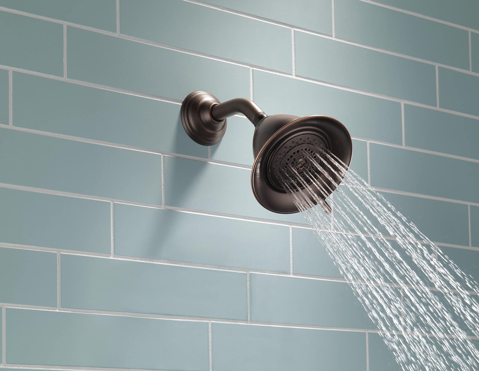 Chrome shower head with curved arm mounted on tile wall, water streaming downward.