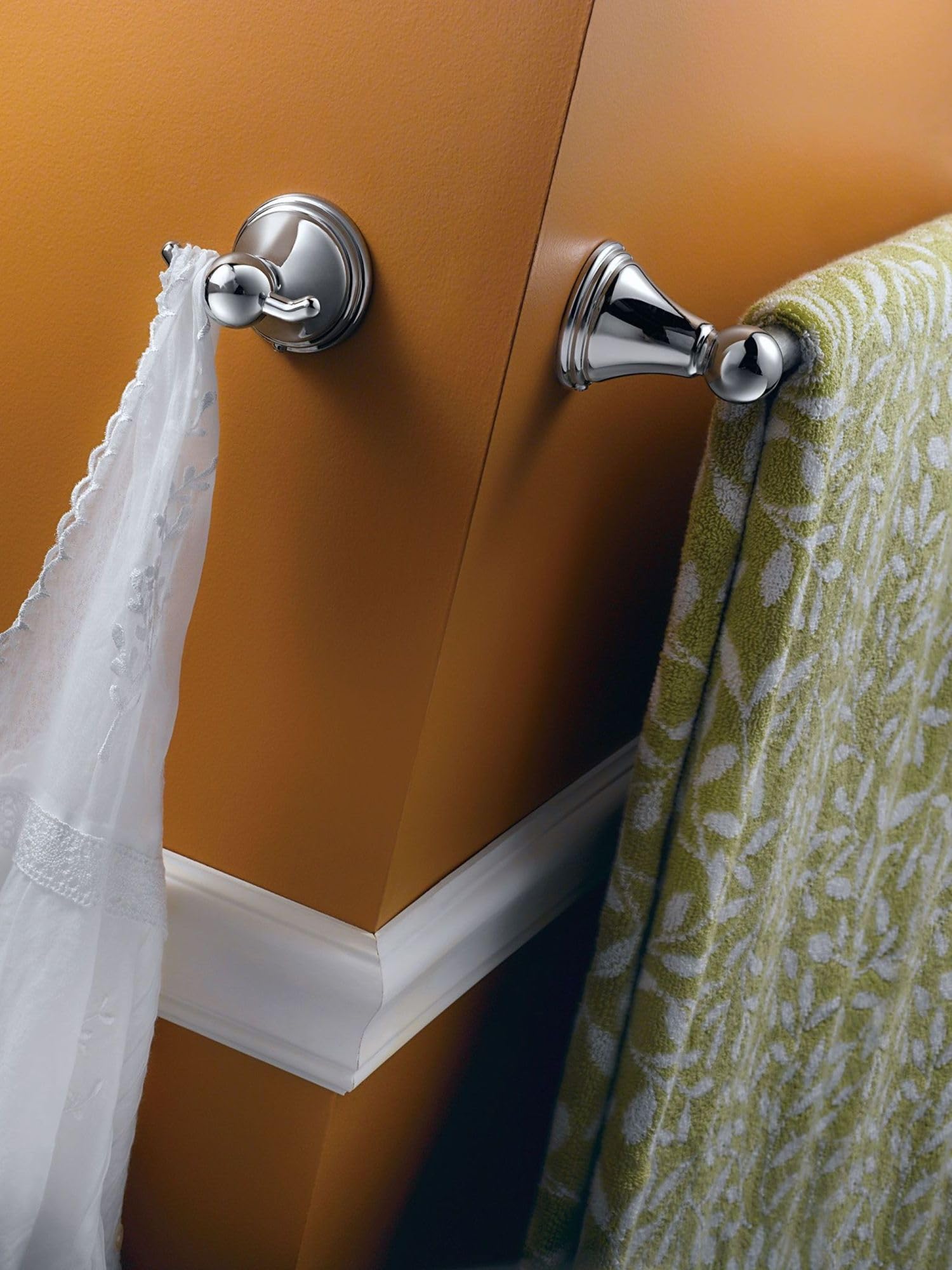 Chrome towel bars mounted on orange wall with white towel on left and green patterned towel on right.