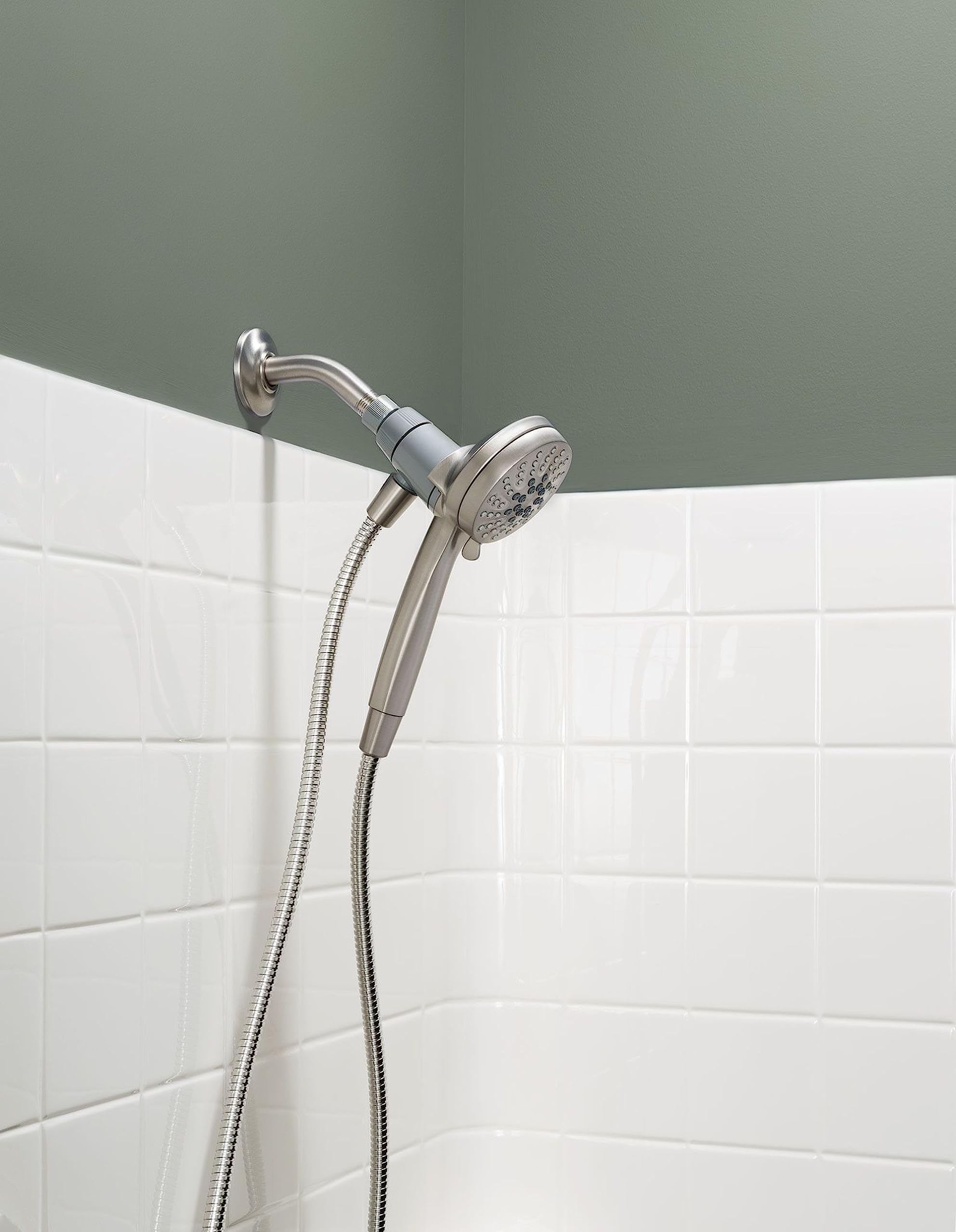Brushed nickel hand shower with flexible hose attached to wall-mounted bracket above white subway tile.