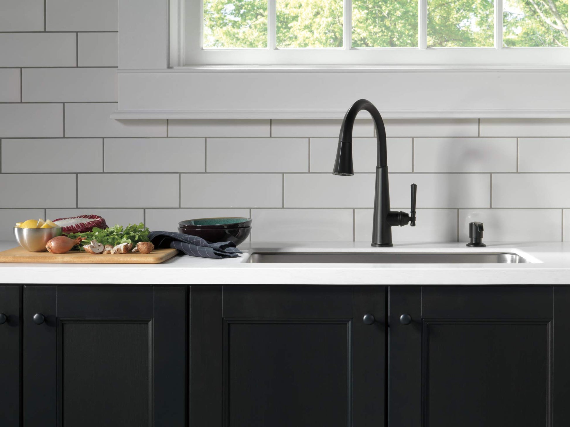 Matte black metal soap dispenser pump mounted on white countertop next to kitchen sink faucet.