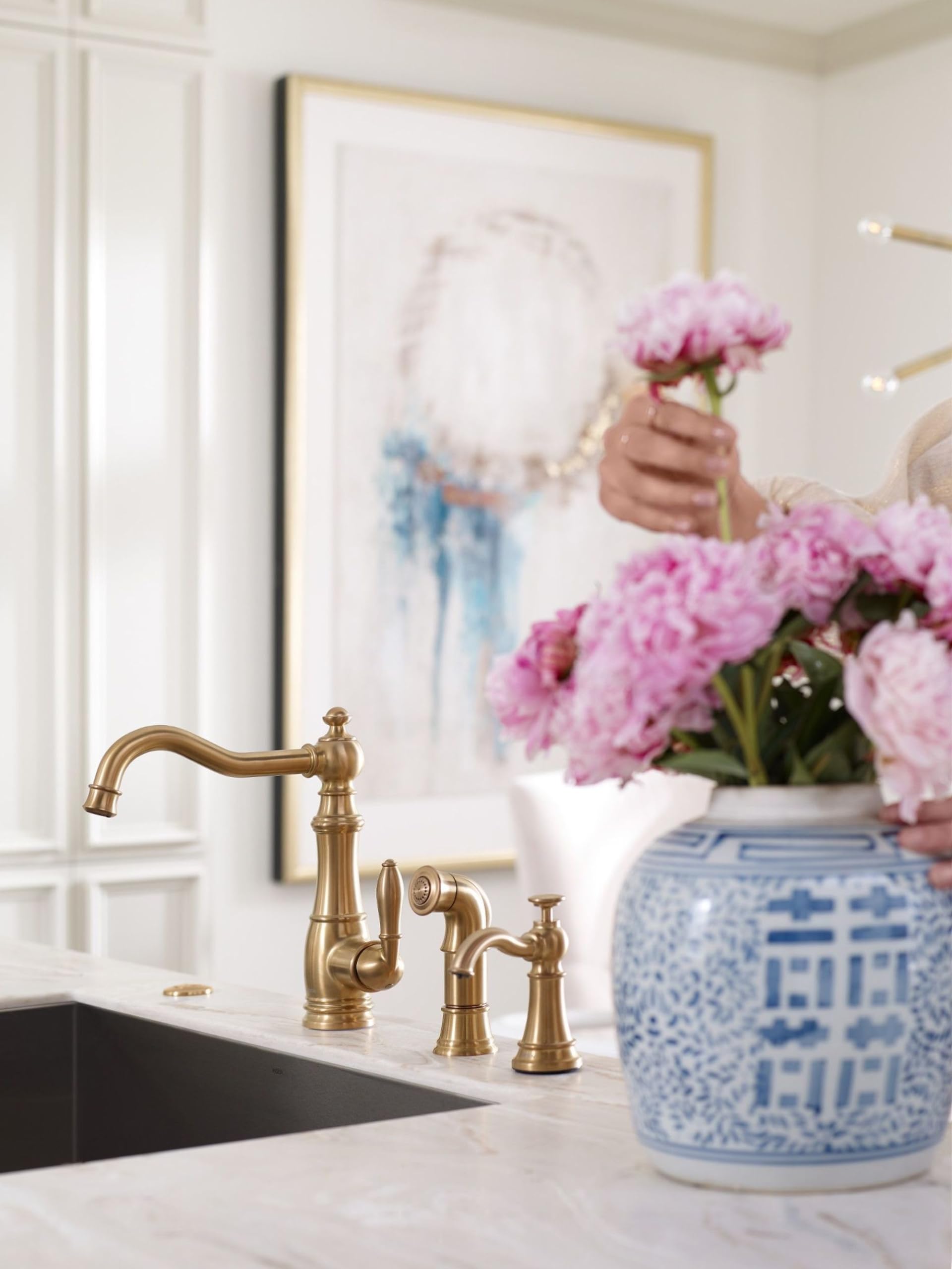 Brushed gold traditional kitchen faucet with matching soap dispenser pump mounted on white countertop next to sink.