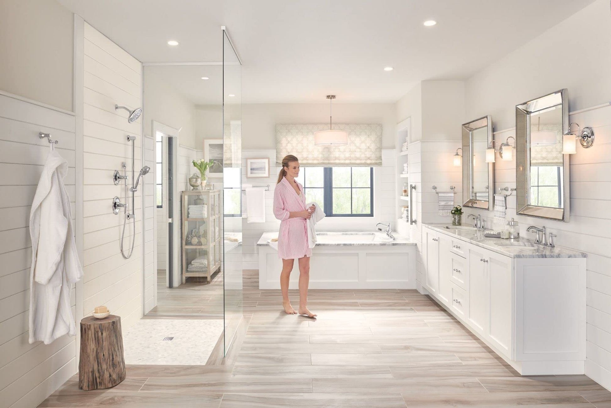 Chrome two-handle deck-mounted Roman tub faucet with hand shower installed on white bathroom tub.