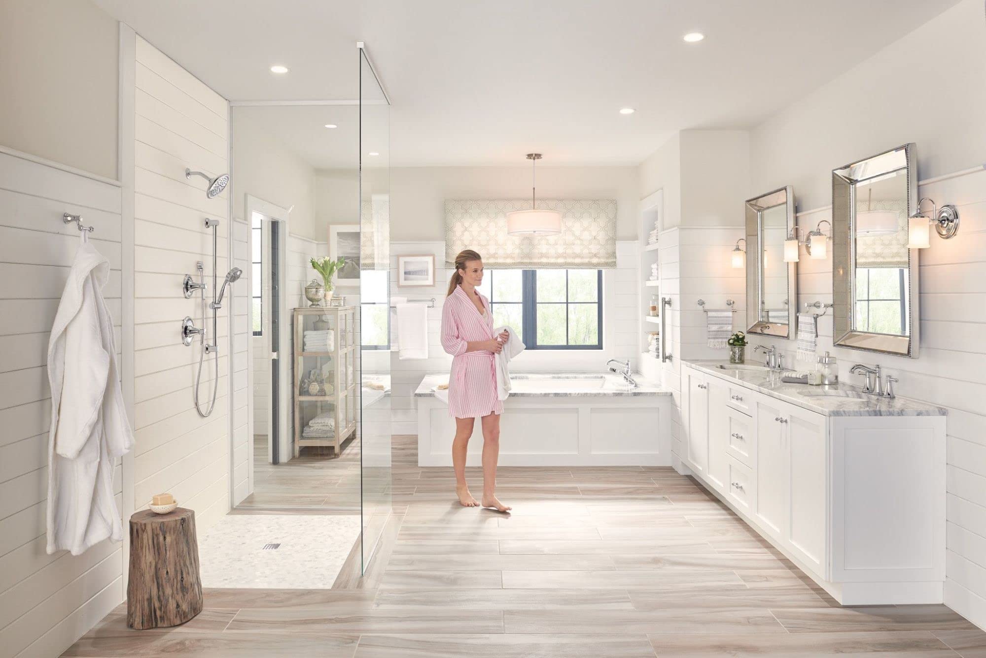 Chrome two-handle deck-mounted Roman tub faucet with hand shower installed on white bathroom tub.