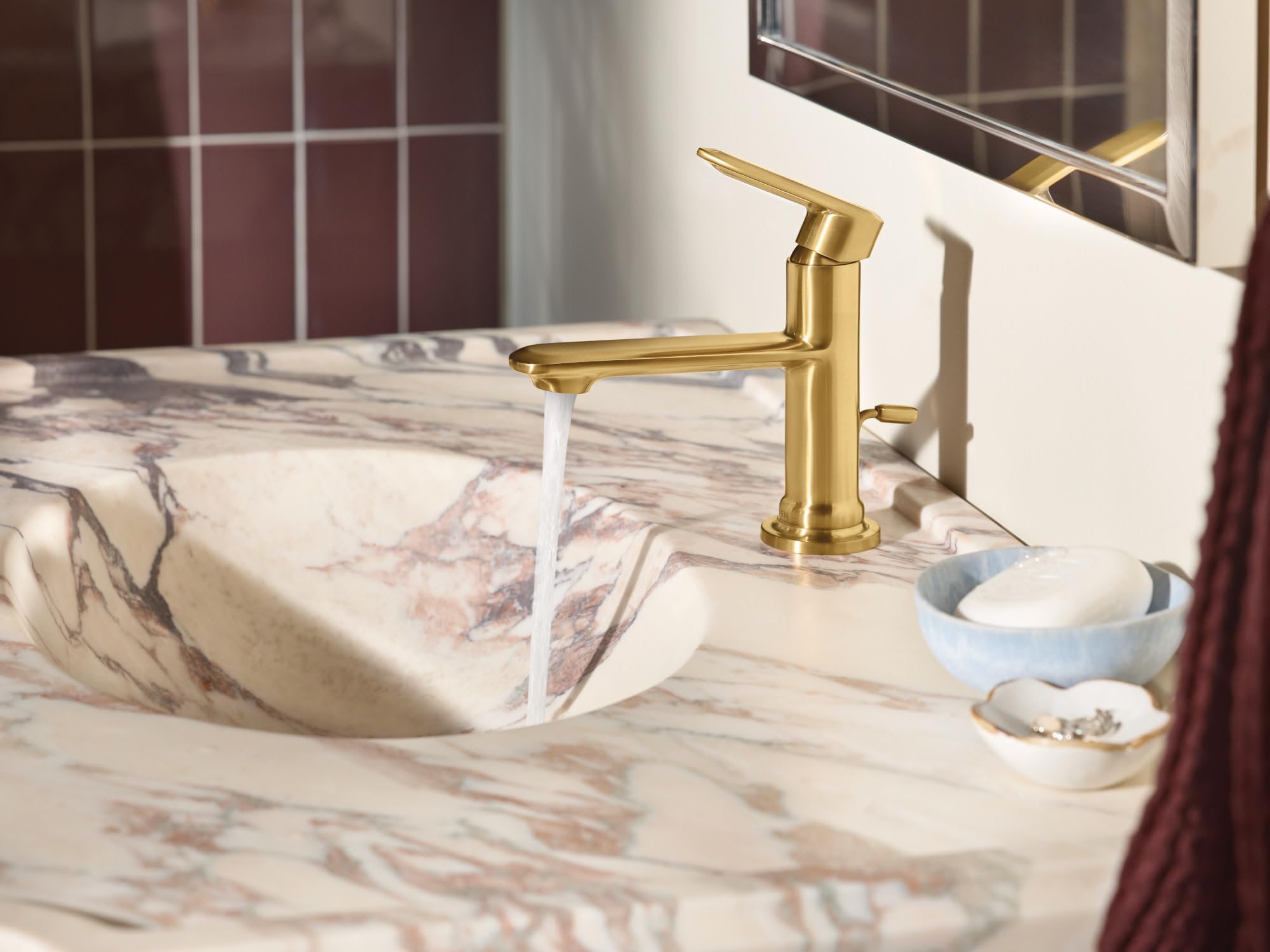 Brushed gold single-handle bathroom faucet with water running into a marble sink.