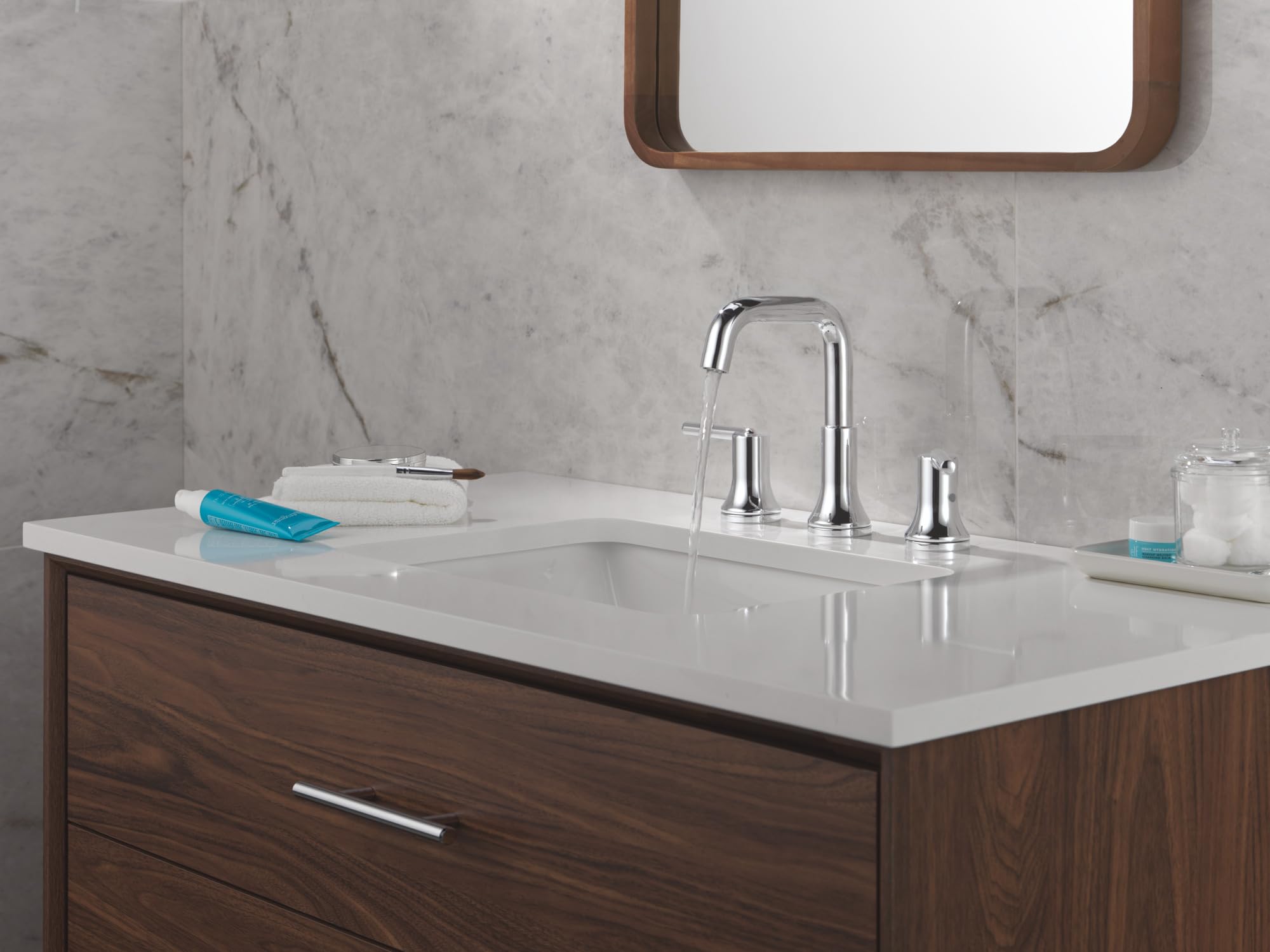 Chrome two-handle widespread bathroom faucet with curved spout installed on white countertop above sink.