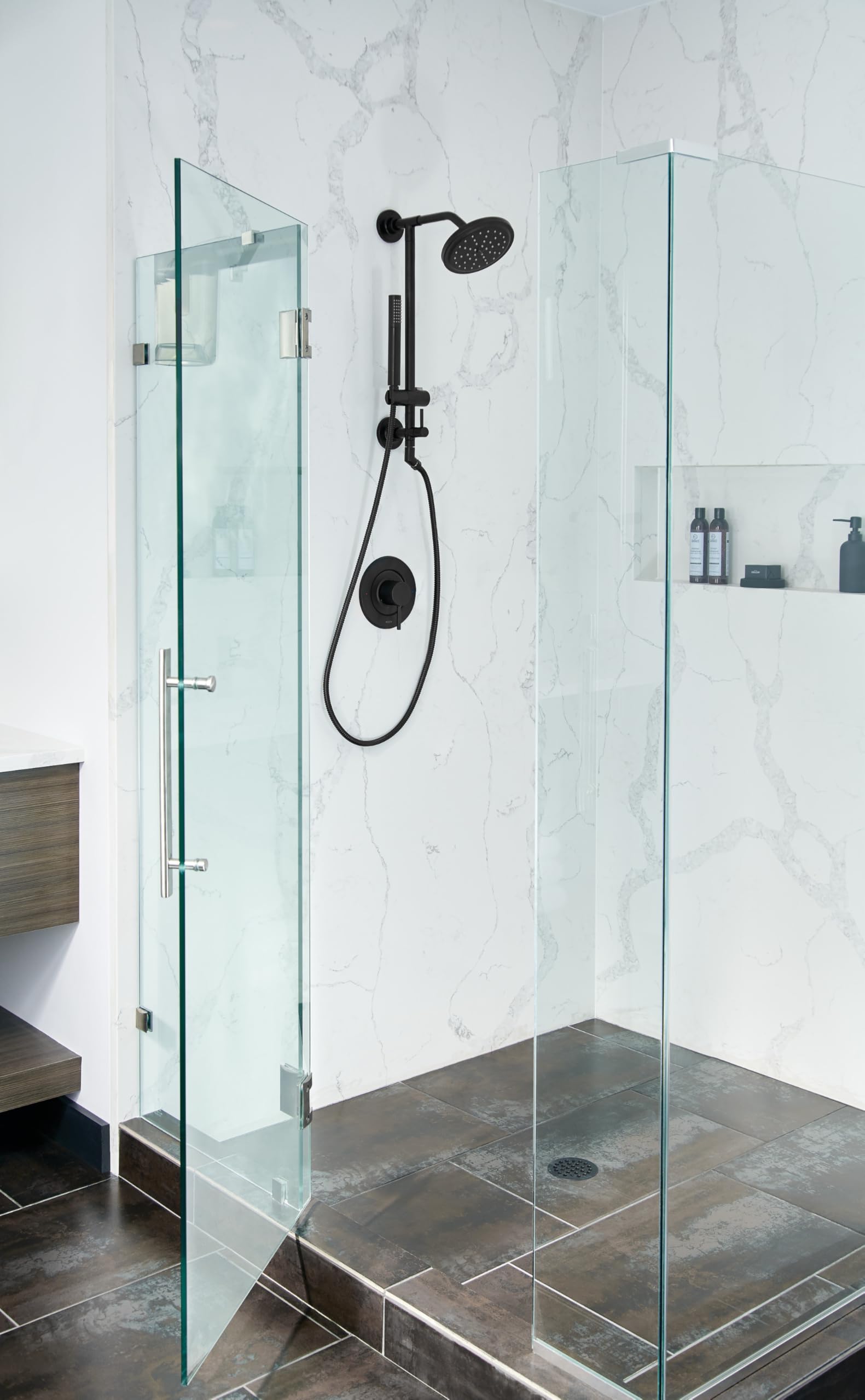 Matte black shower valve trim kit with single handle, showerhead, and handheld spray mounted on marble tile wall.