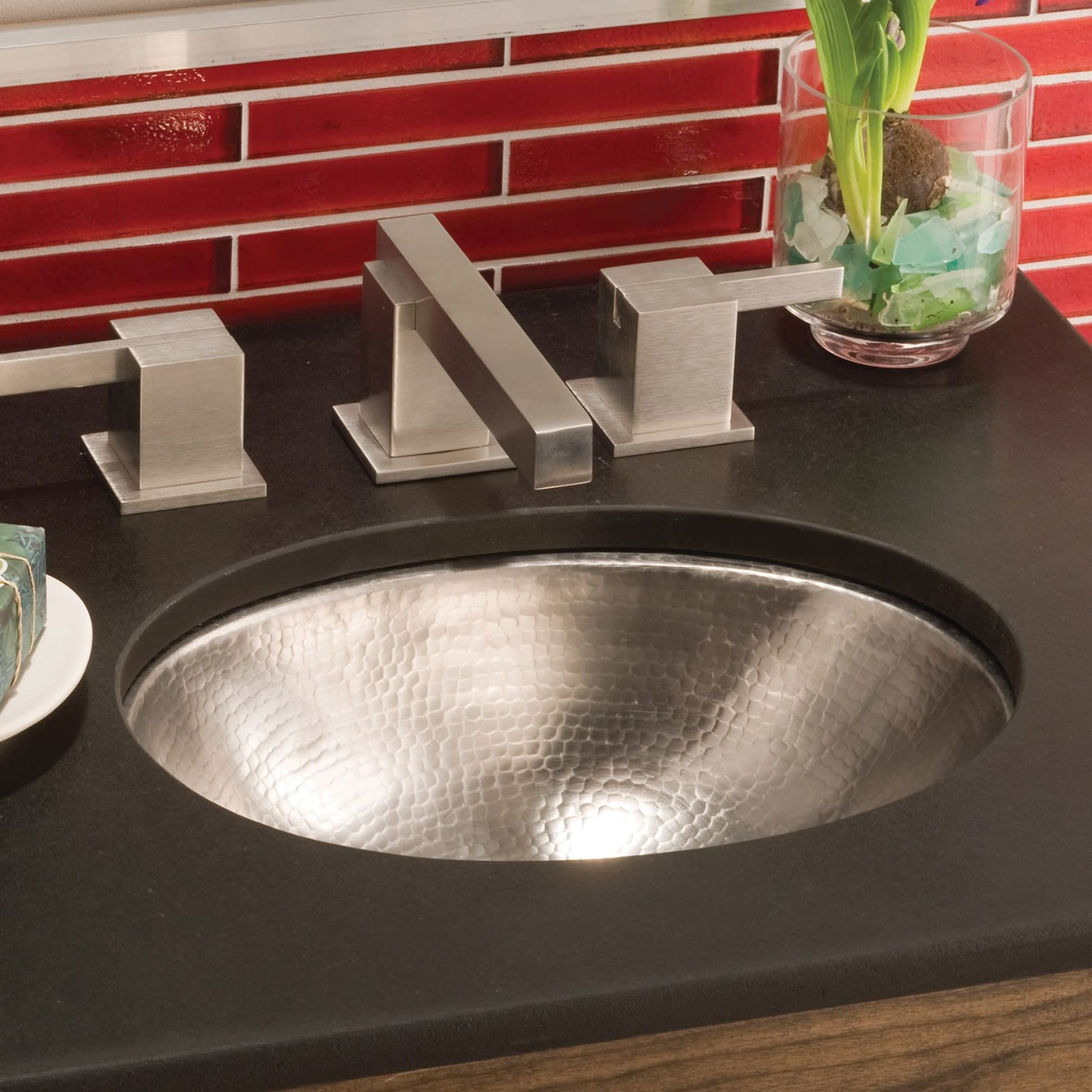 Polished nickel faucet with geometric handles installed above hammered metal undermount sink in dark countertop.