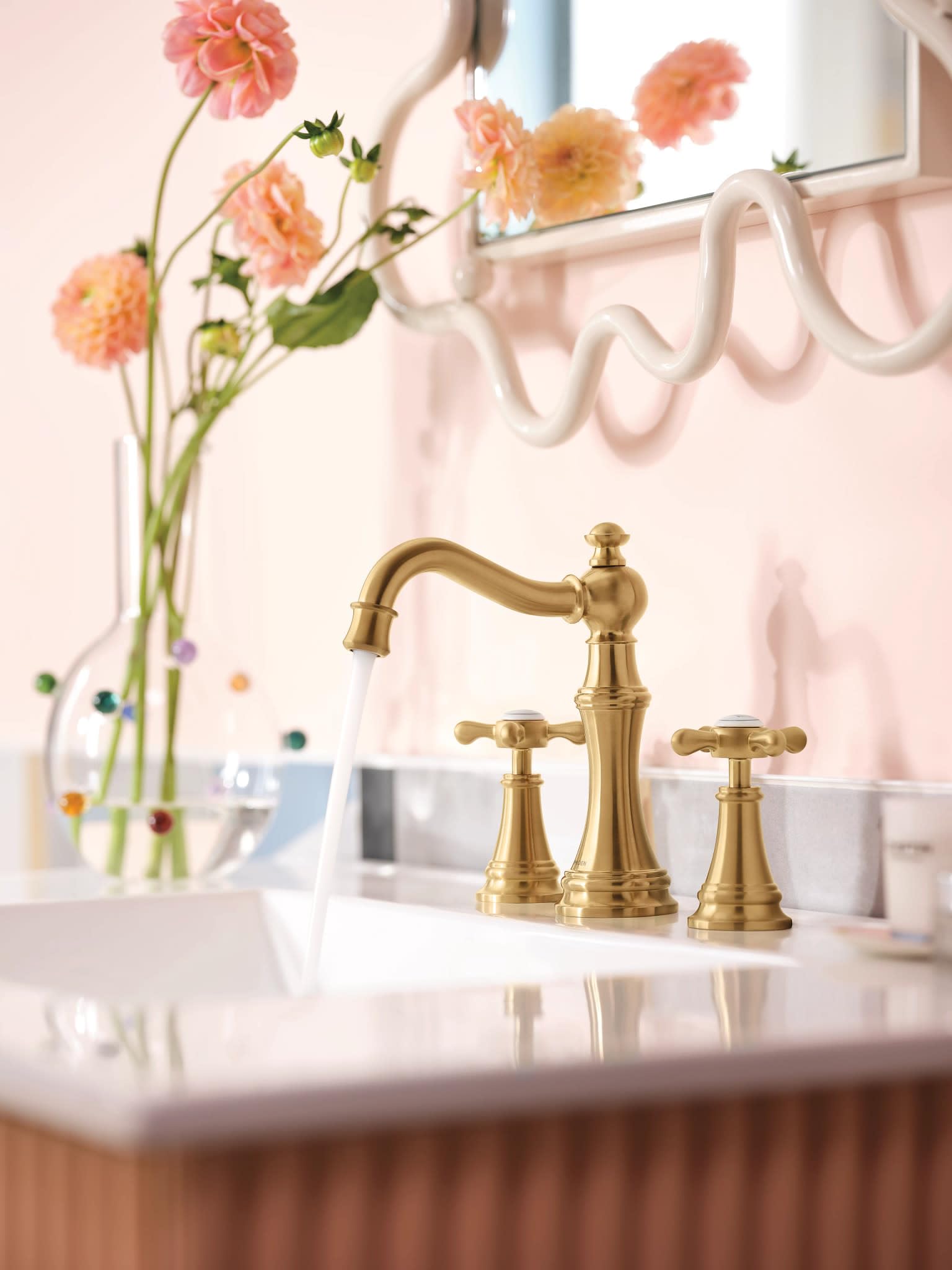Brushed gold two-handle widespread bathroom faucet with curved spout and cross handles on white sink.